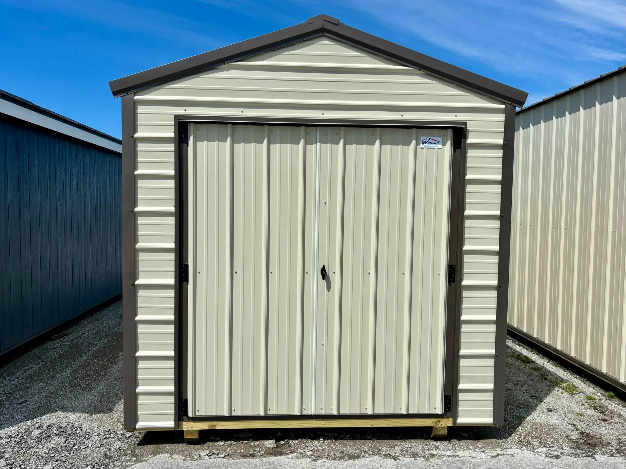 A stone colored metal shed with double doors and bronze trim.