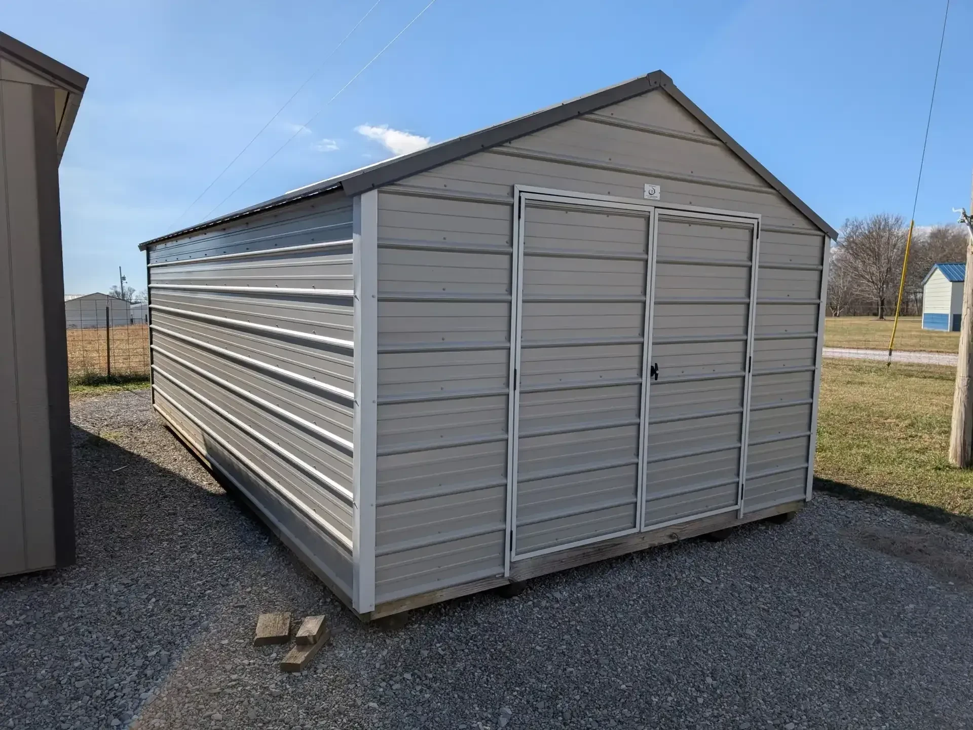 a gray metal utility shed with white trim and dark gray roof. It has double doors