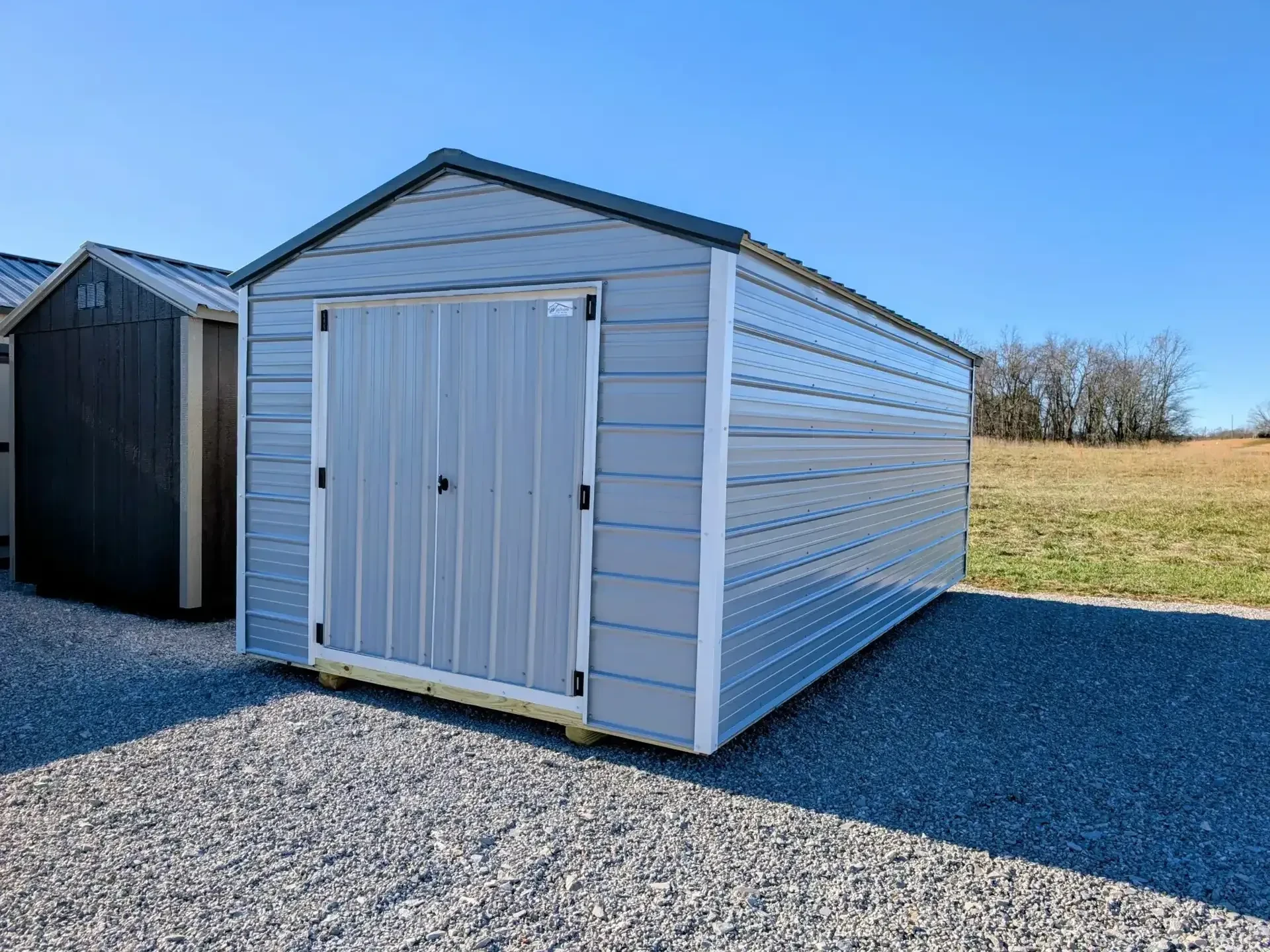 a gray metal utility shed with double doors. It has white trim and a slate gray colored metal roof