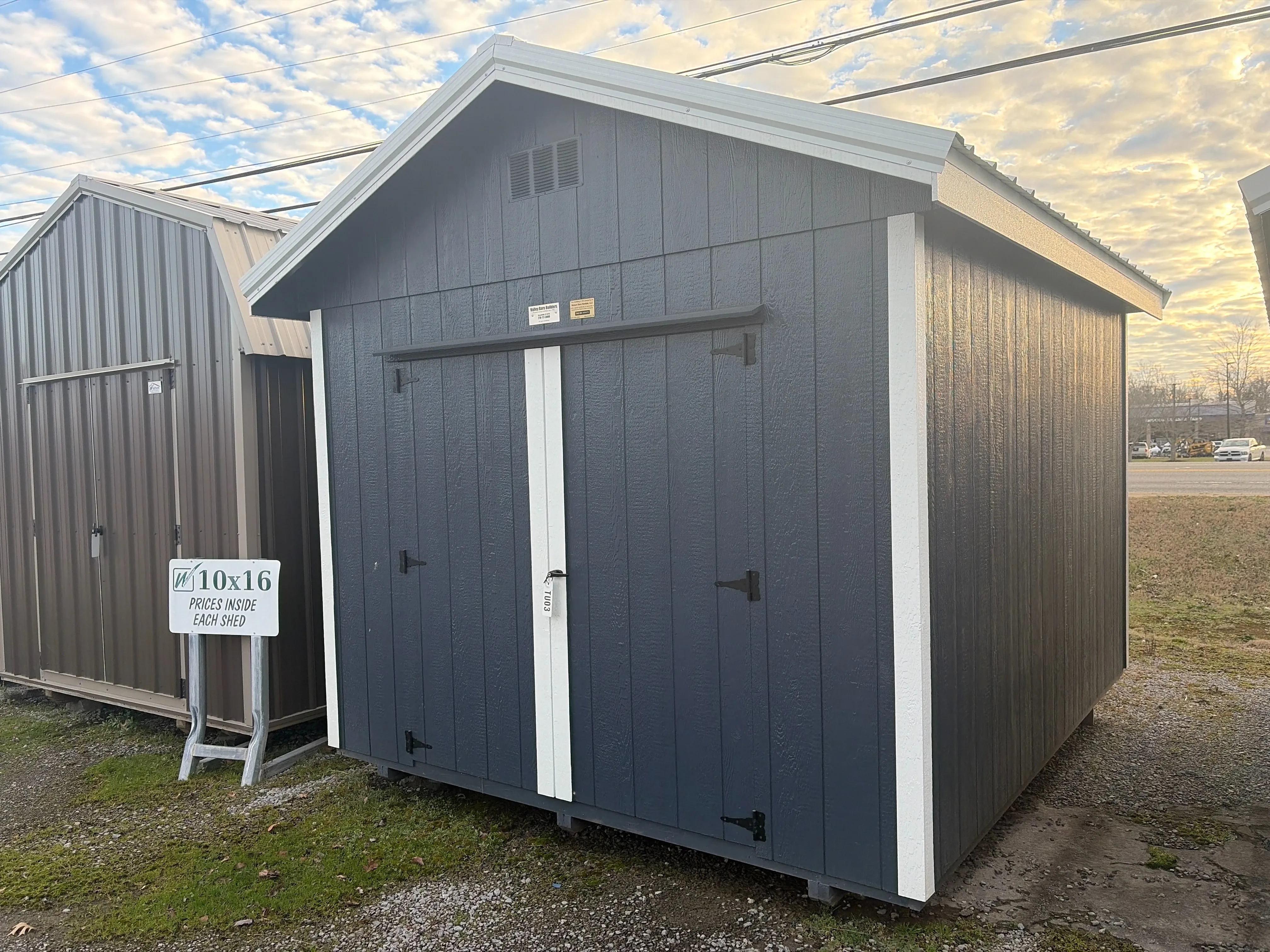 a blue wood utility shed with double doors and white trim. It has a roof overhang on all sides