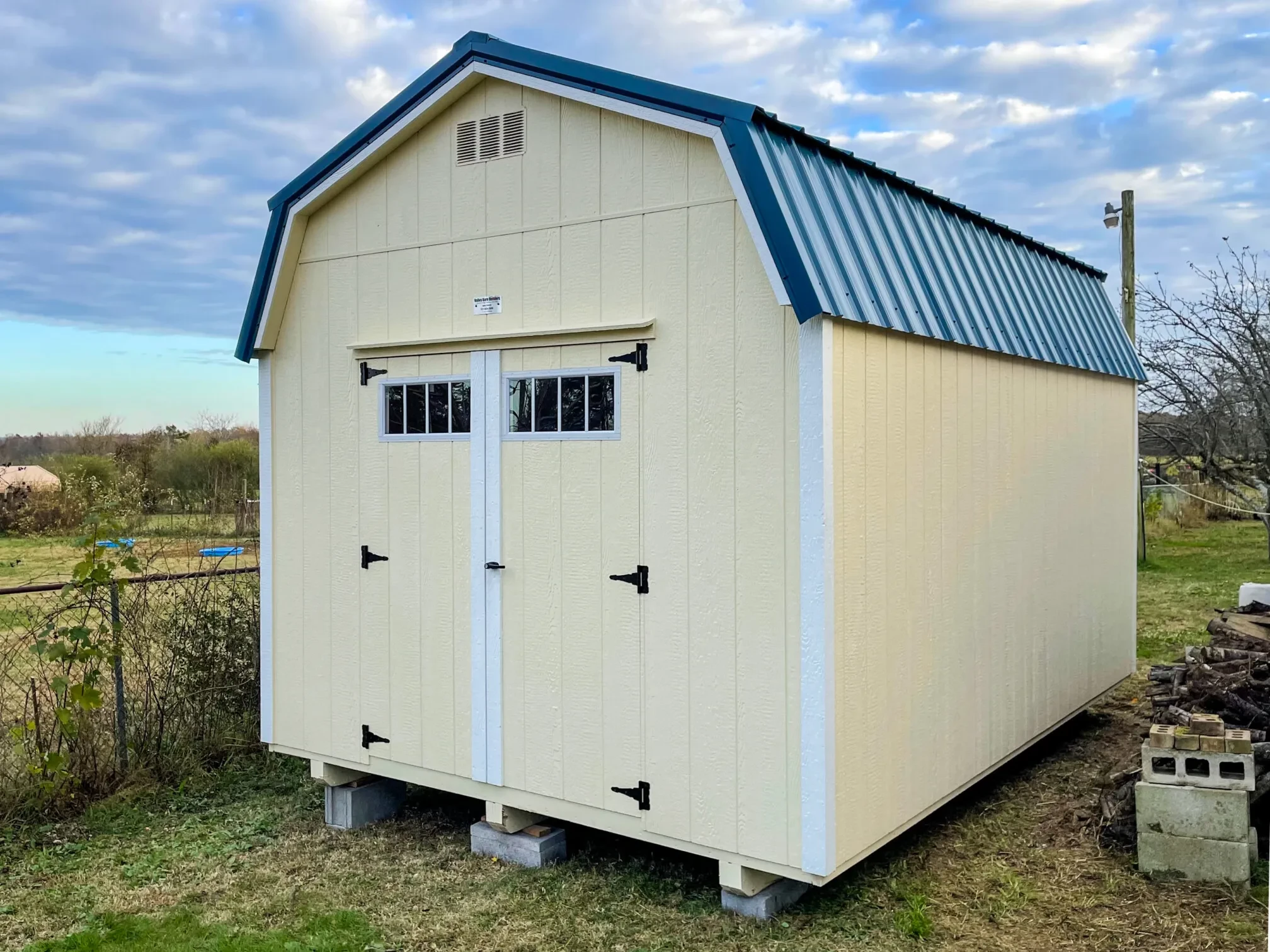 a cream colored wood shed with a blue metal roof and double doors with transom windows in the front