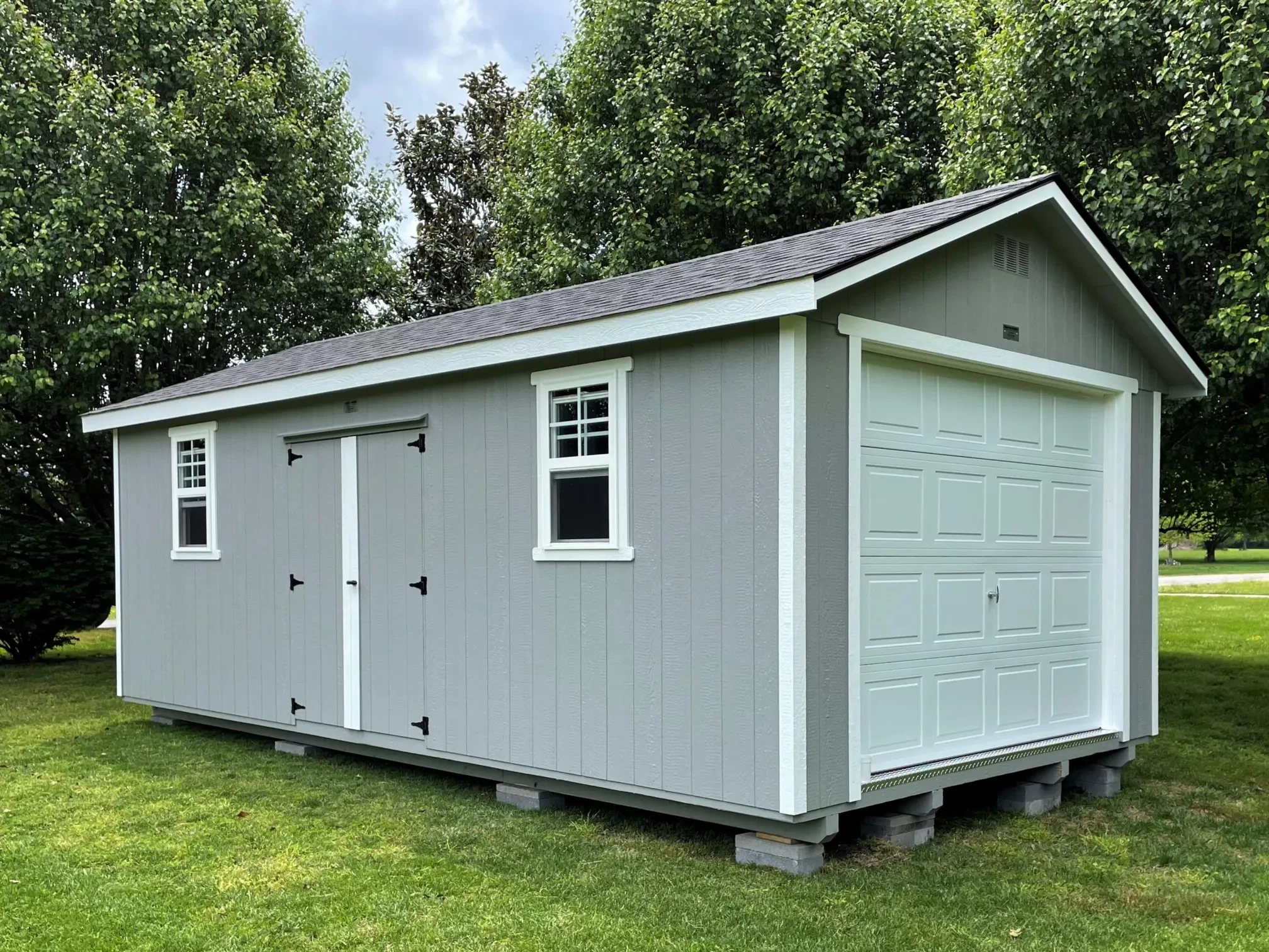 a large gray garage shed with a garage door in the end and double doors and two windows in the side