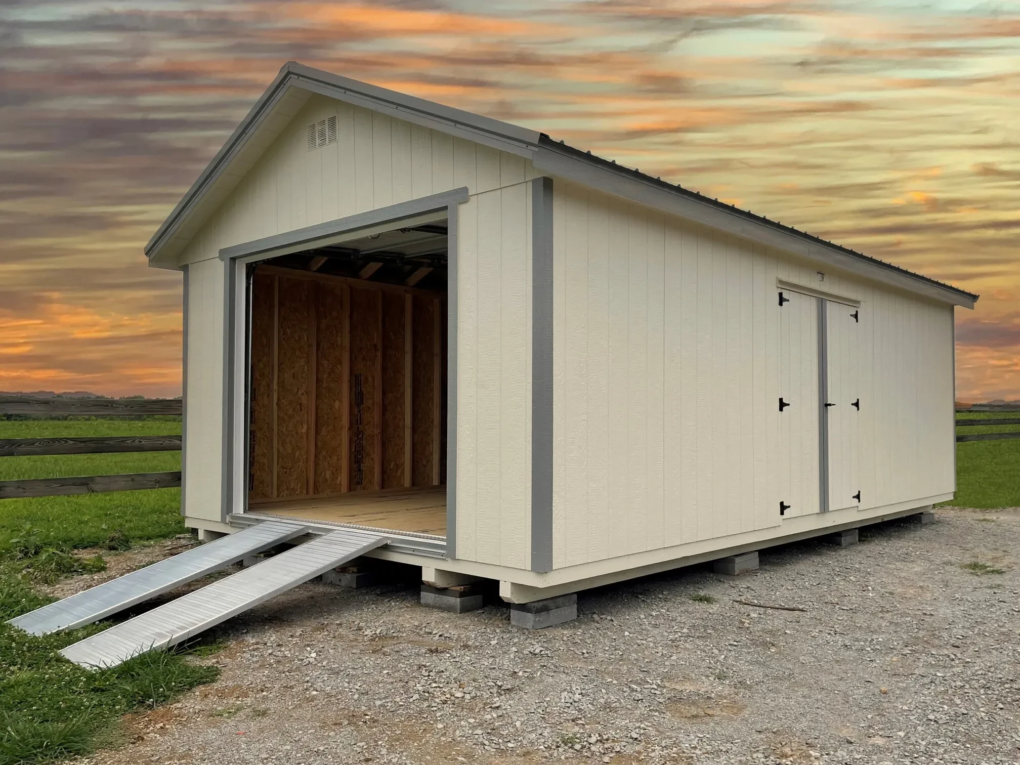 A large tan shed with an open garage door on the end and a ramp attached to the shed with a colorful sky in the background