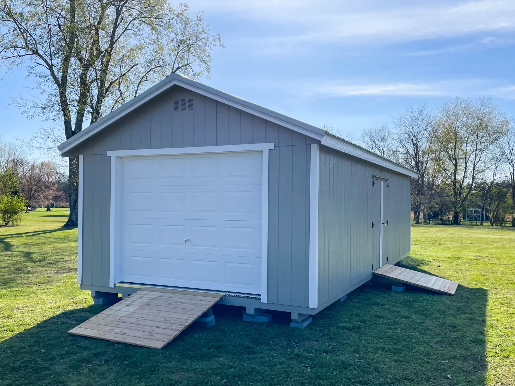 a large garage shed with a garage door in the end and double doors in the side with ramps at both doors