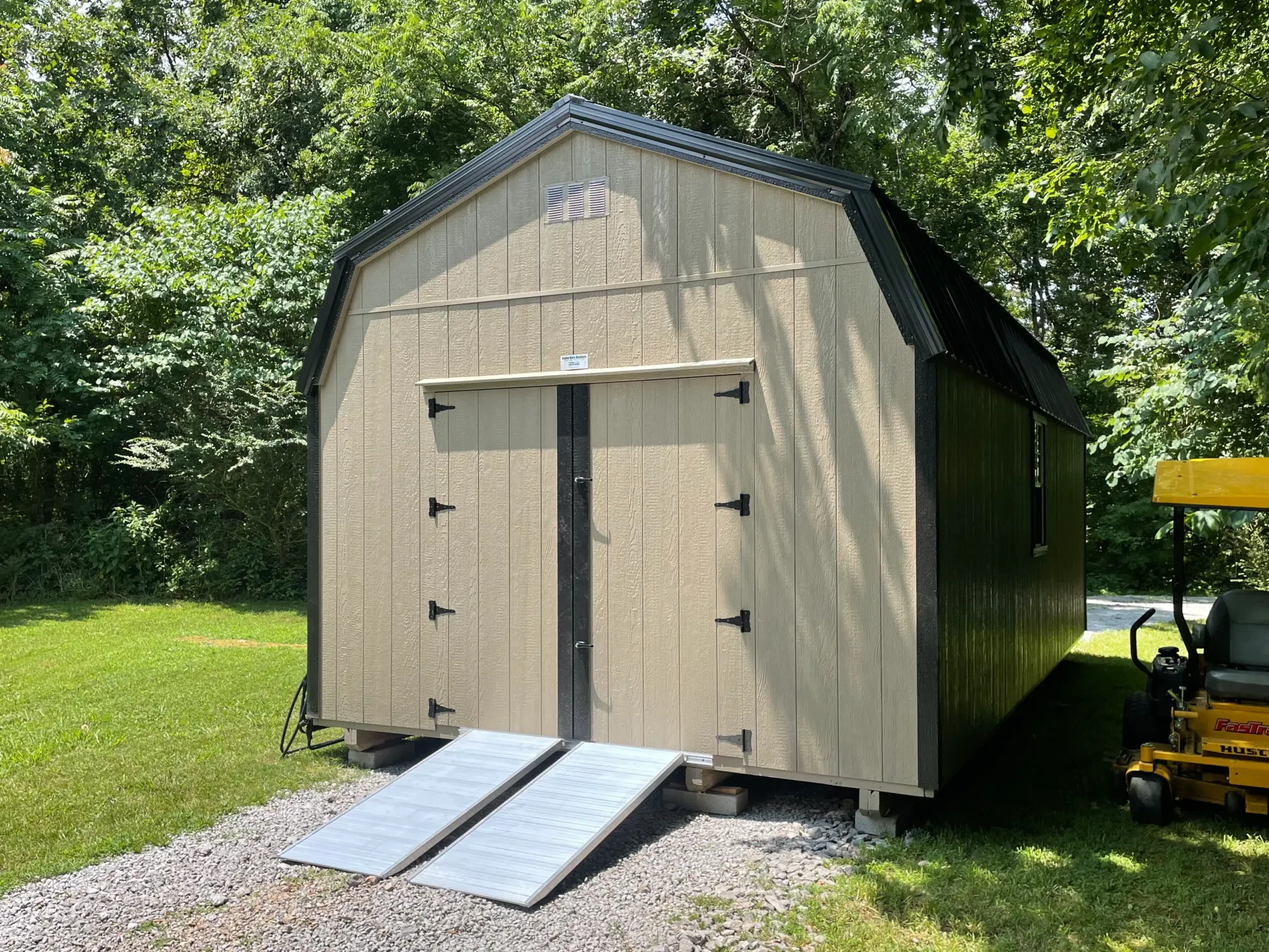 A large lofted barn with double doors in the end with a set of ramps. There is a riding mower beside the shed