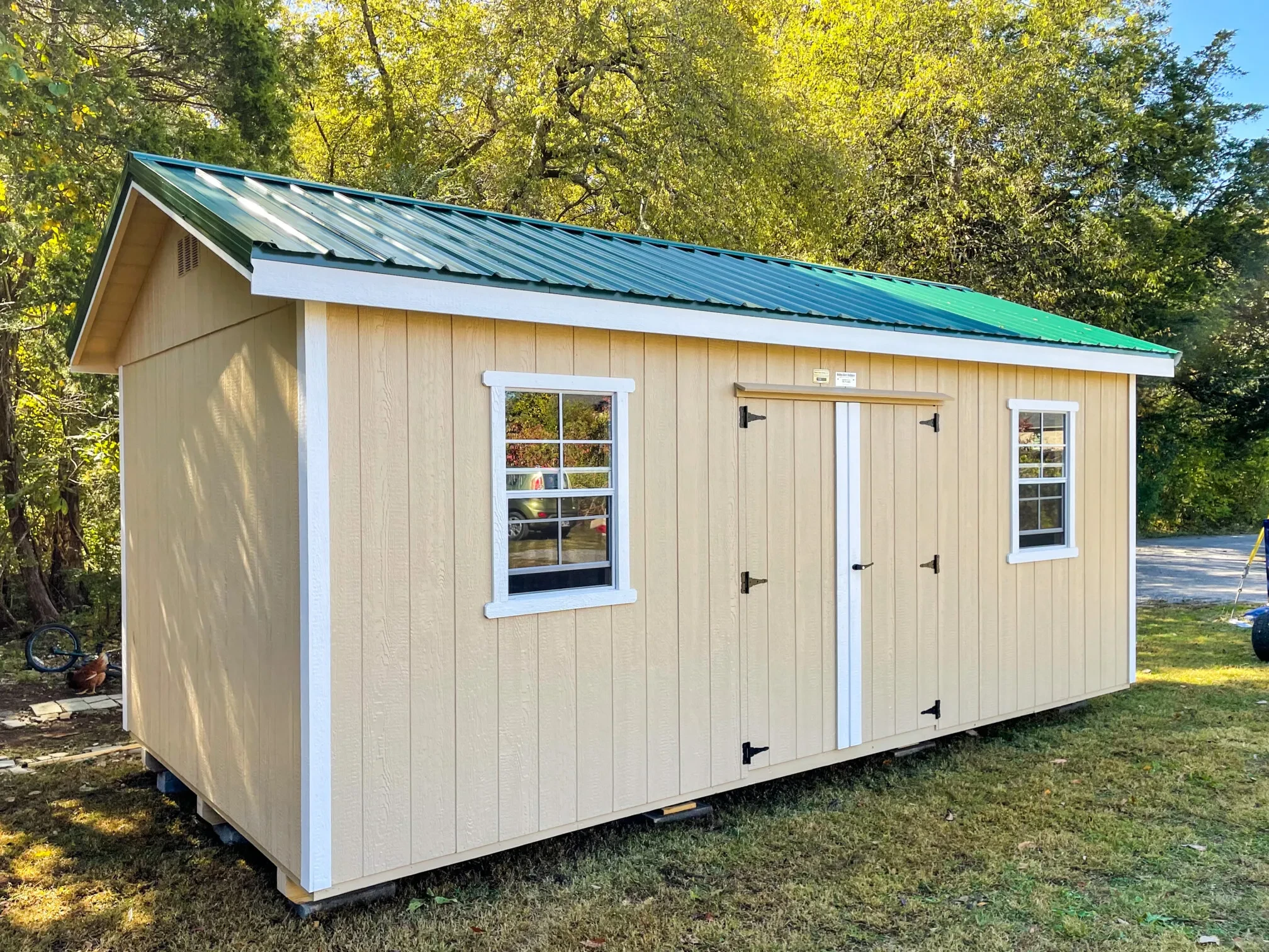 a cream colored shed with a green roof and double doors and two windows