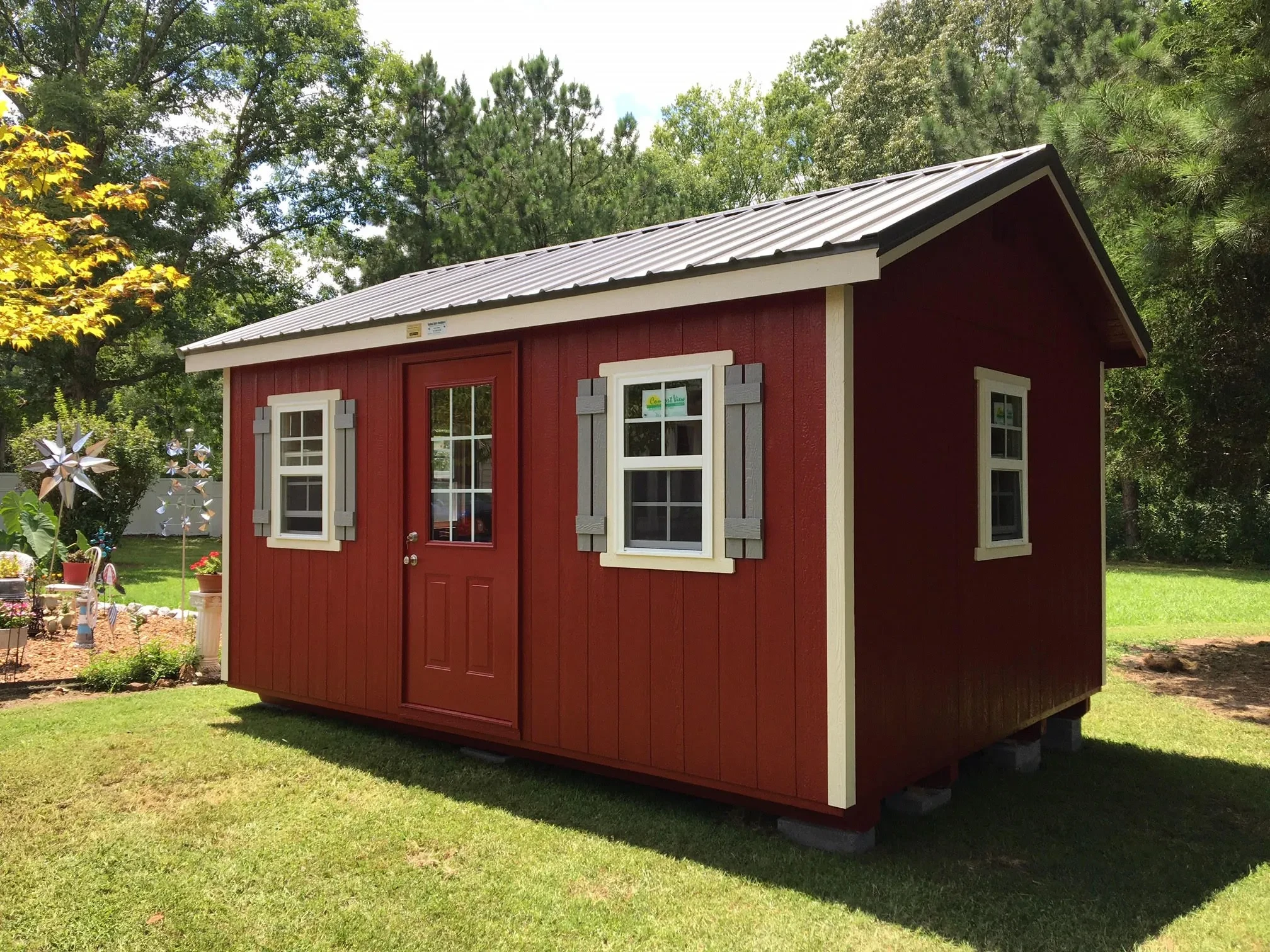 A dark red wood shed with white trim and multiple windows with shutters