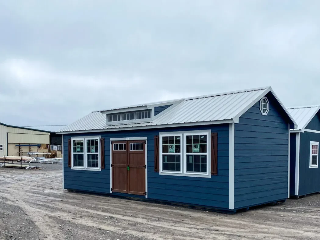 A large shed with dark blue lap siding, white trim, and accenting wood shutters and doors with many windows