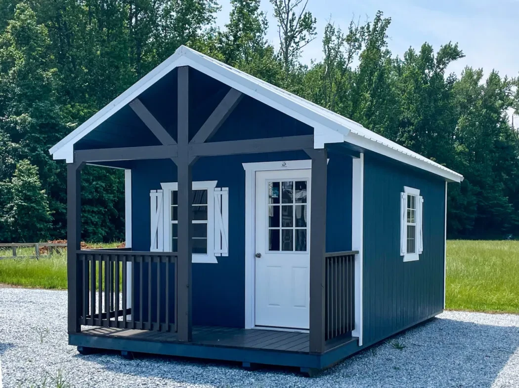 a dark blue shed with white roof, trim, doors, and windows and a black porch on the front of the building