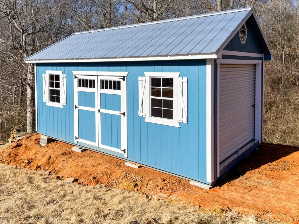 a light blue shed with a grage door in the end and double doors and two windows in the side