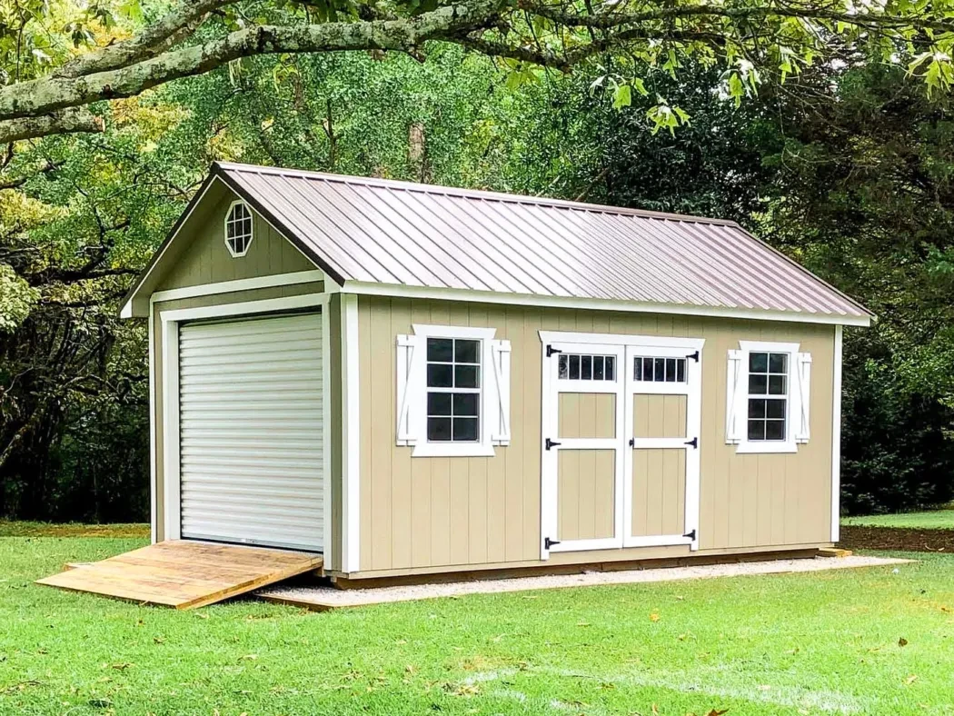 a large tan shed with a brown roof and white trim with a garage door and ramp on the end