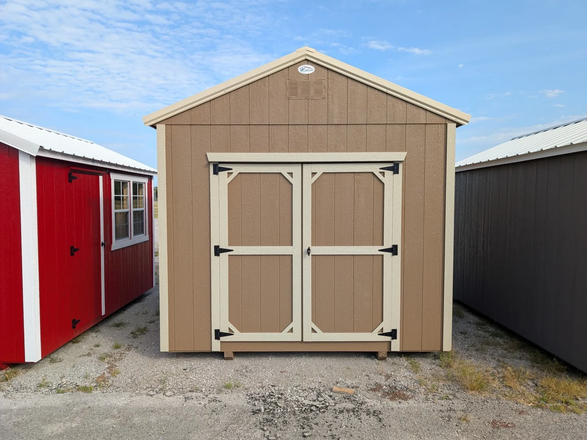 A frontal view of a shed that is light stone in color, between two other sheds