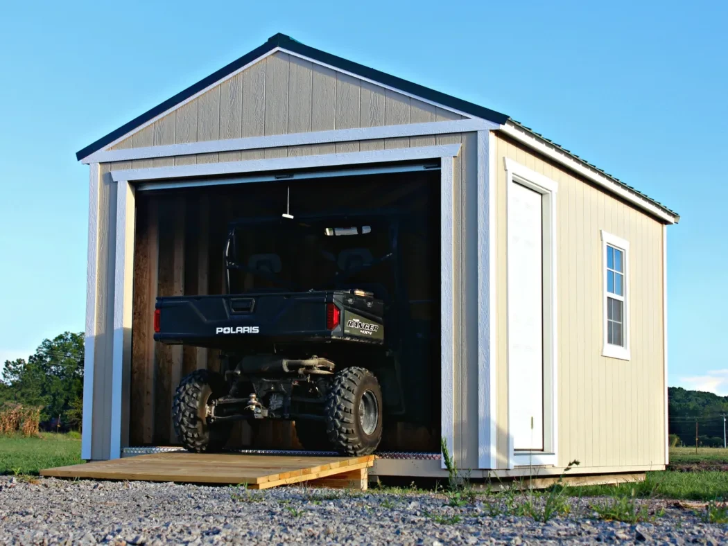 A wood shed with an open garage door in the end and an atv parked inside