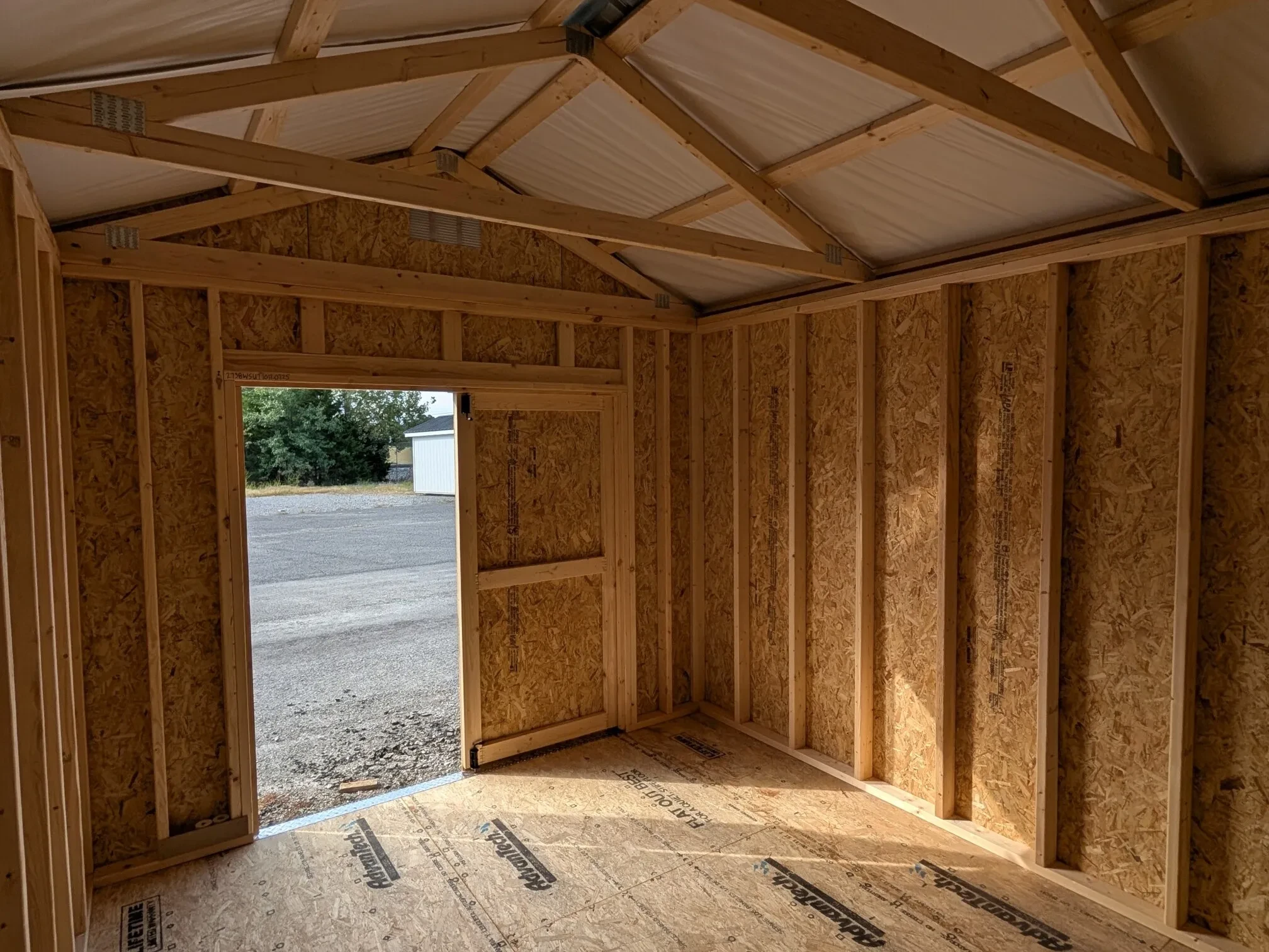 The inside view of a wooden shed looking out through the double doors that are open.