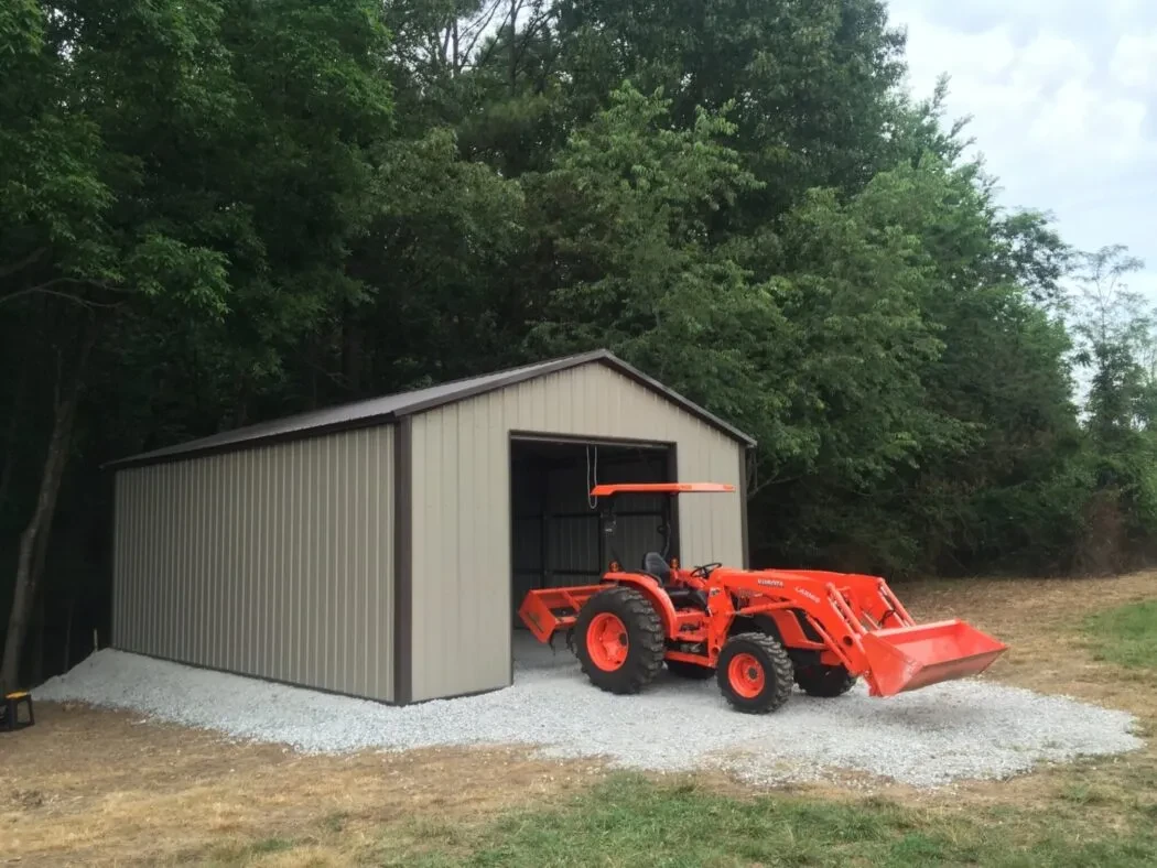 A tan and brown metal garage with a bright orange tractor pulling through a garage door in the end