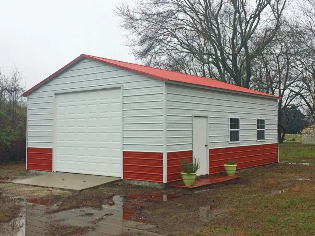 A metal garage with white walls and a red roof and wainscot with a garage door, walk-in door, and two windows