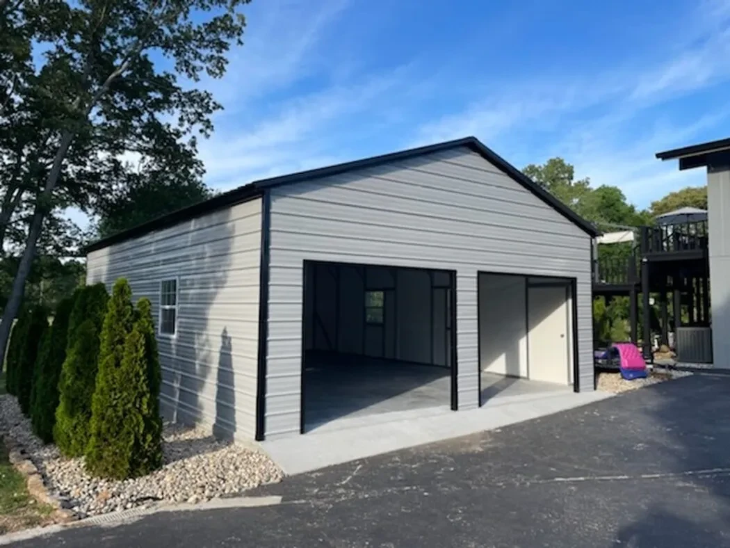 A nicely landscaped white and black garage with two garage doors in the end