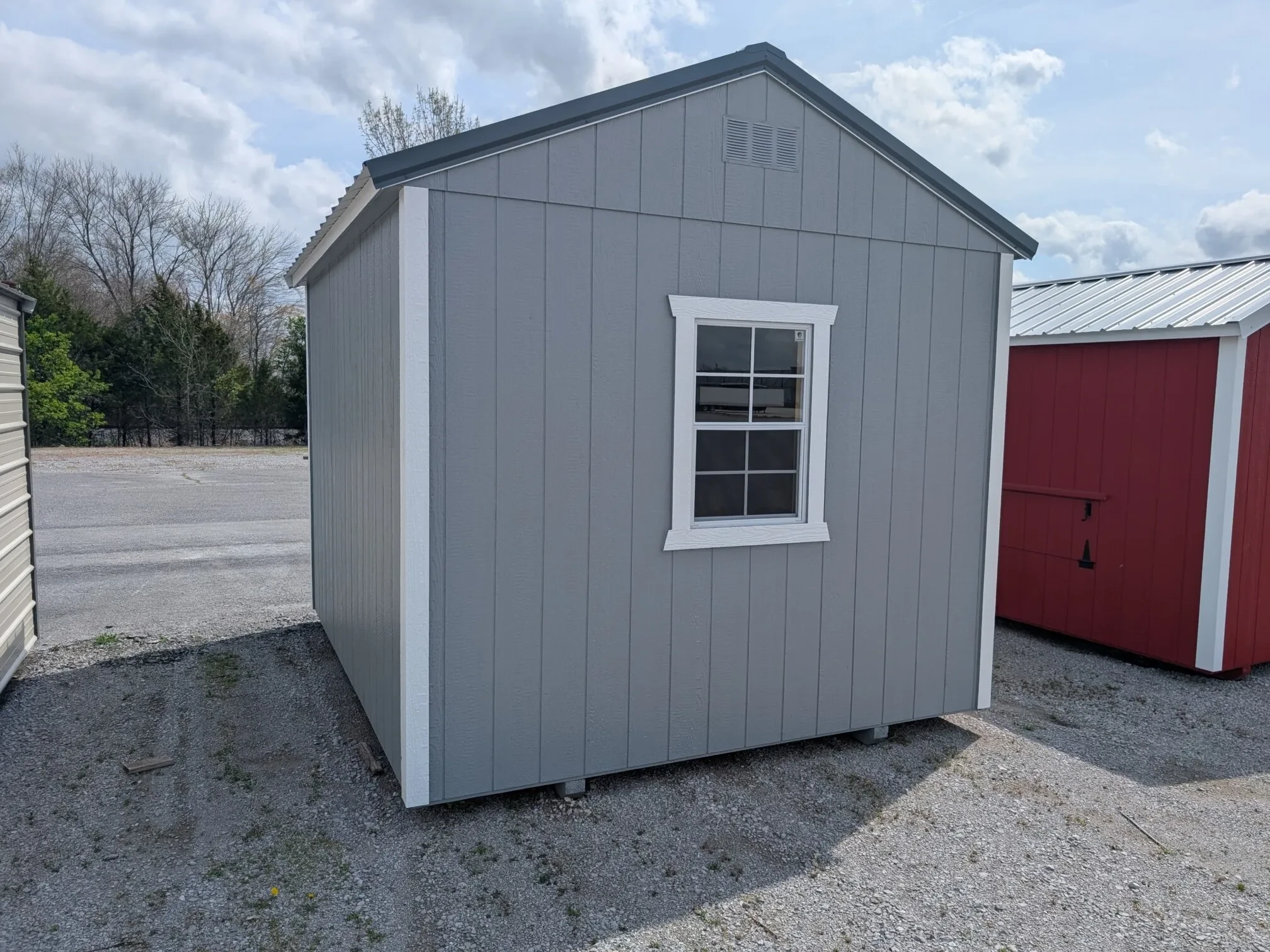 The rear view of a gray wood shed, showing a window in the middle of the back wall