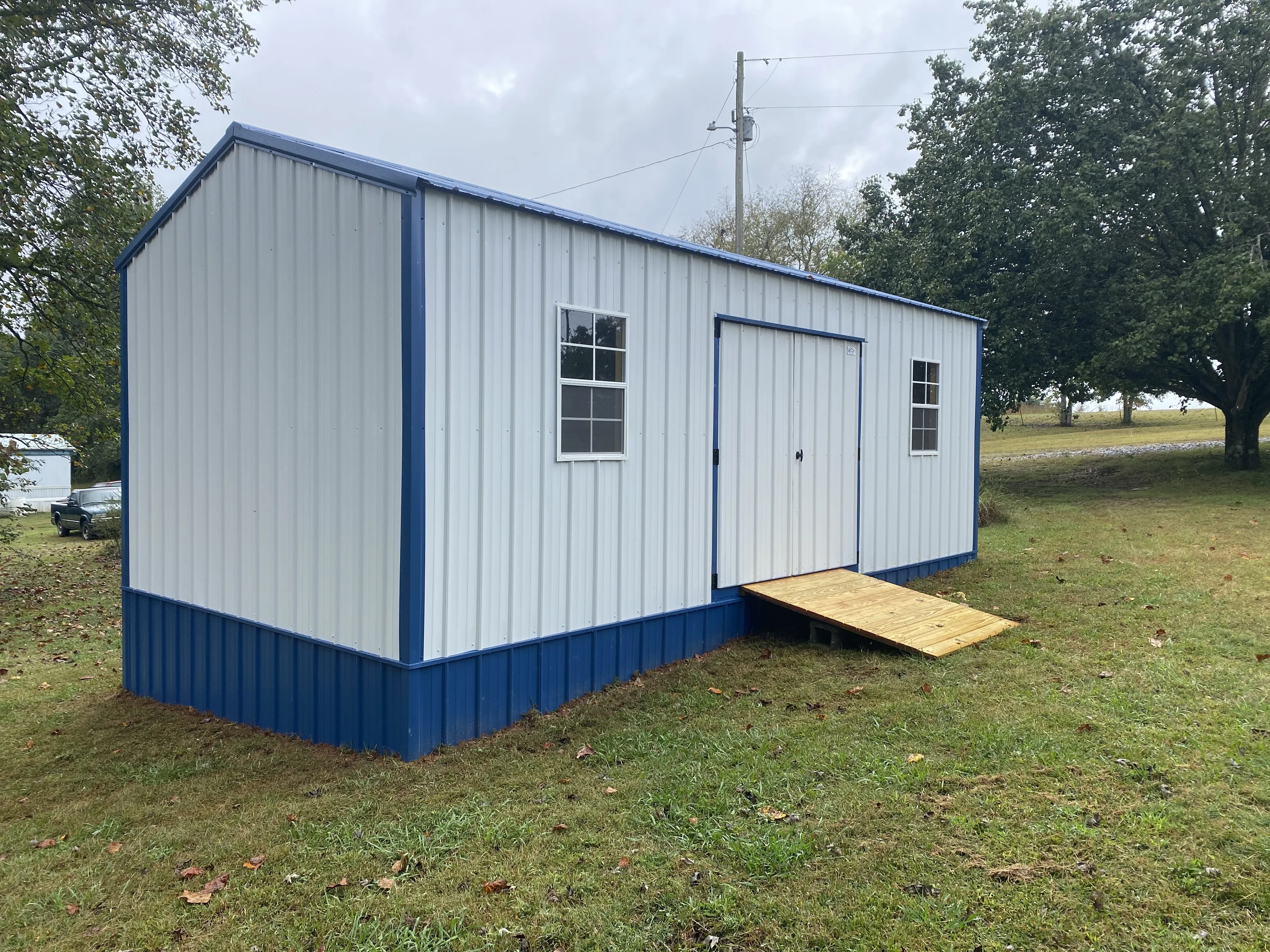 Blue and white metal shed with underpinning and a ramp
