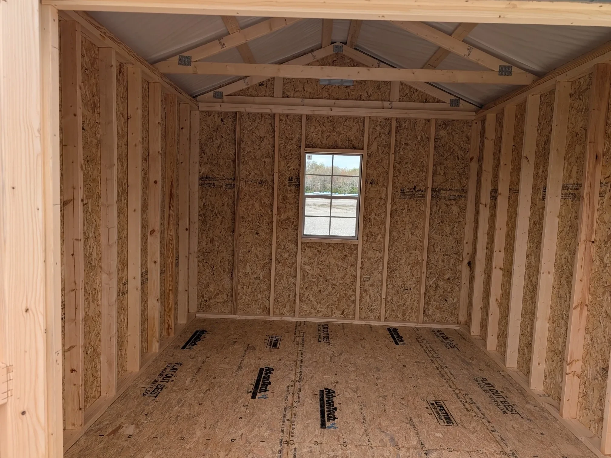 The inside view of a wood shed, it shows the floor, walls, and roof, as well as a window in the middle of the back wall.