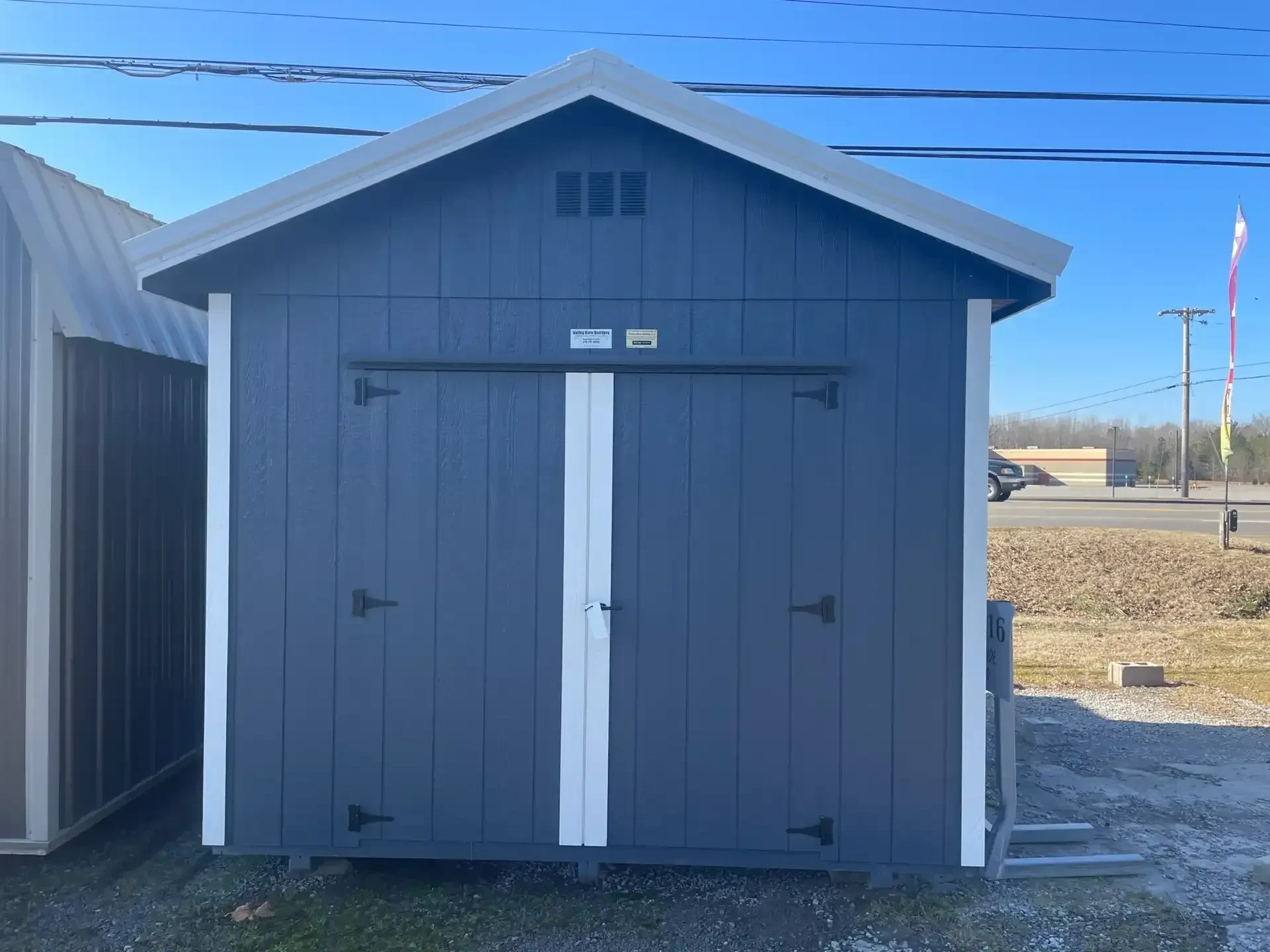 the a blue utility shed with double doors and a roof overhang, it also has white roof trim and white wall trim