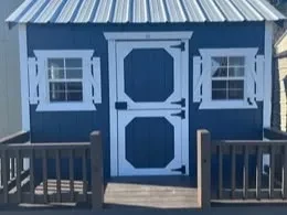 the front of a blue playhouse with white trim. It has a door split in half horizontally and a white metal roof