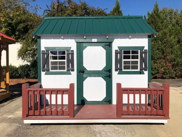 a wood playhouse that is painted white with green trim. It has windows with green shutters
