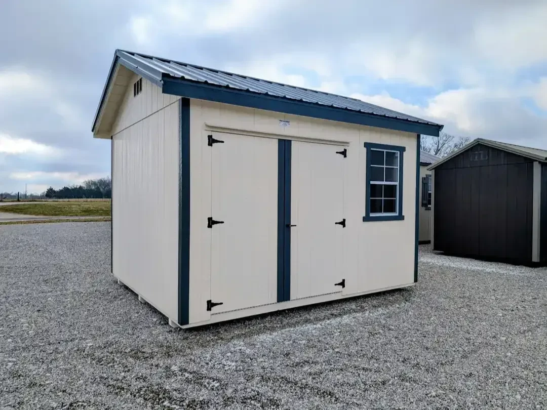 a wood garden shed painted a navajo white color with slate gray trim and a metal slate gray colored roof