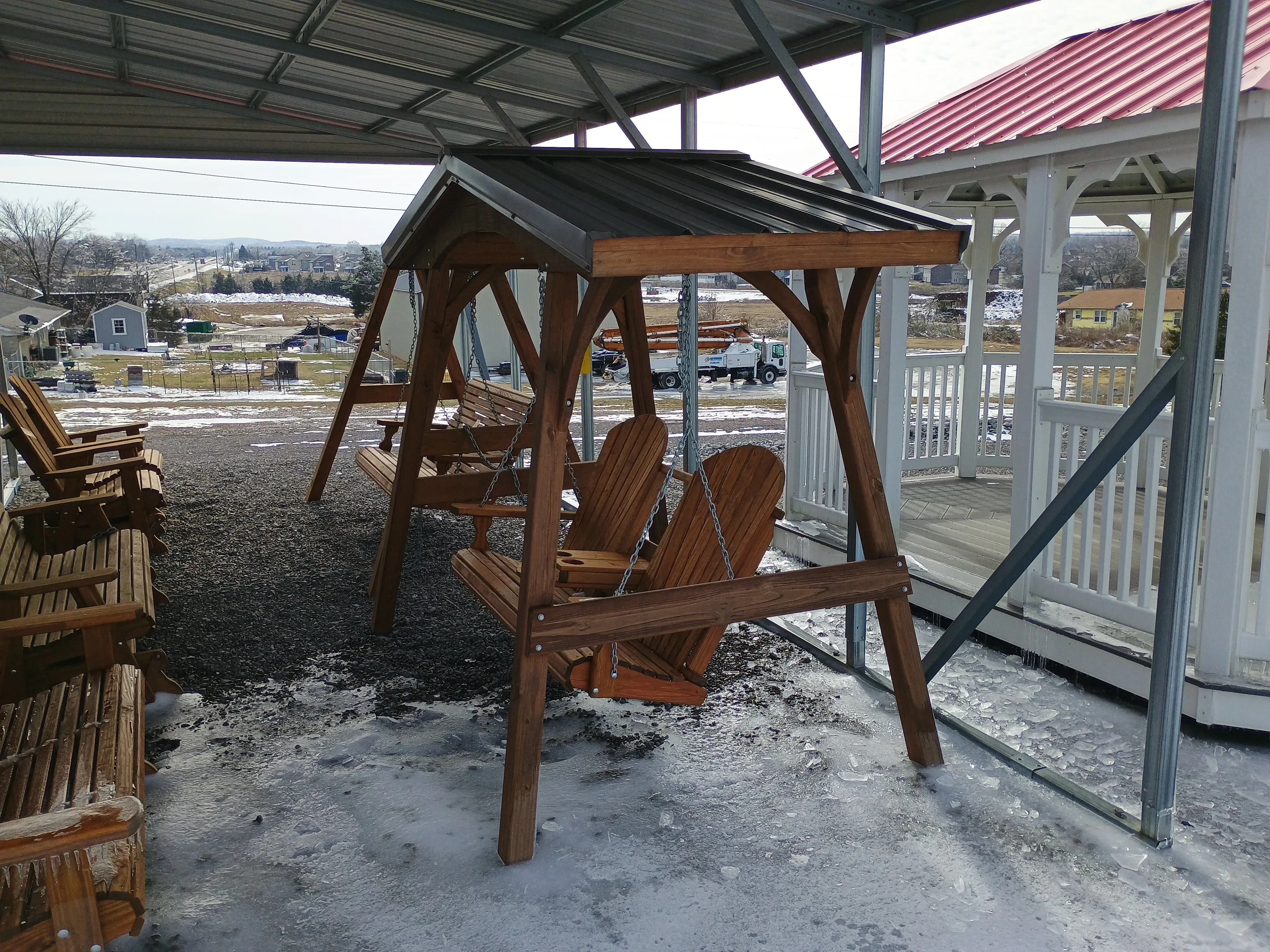 a swing cover with a metal roof, it is holding up a stained wood bench swing