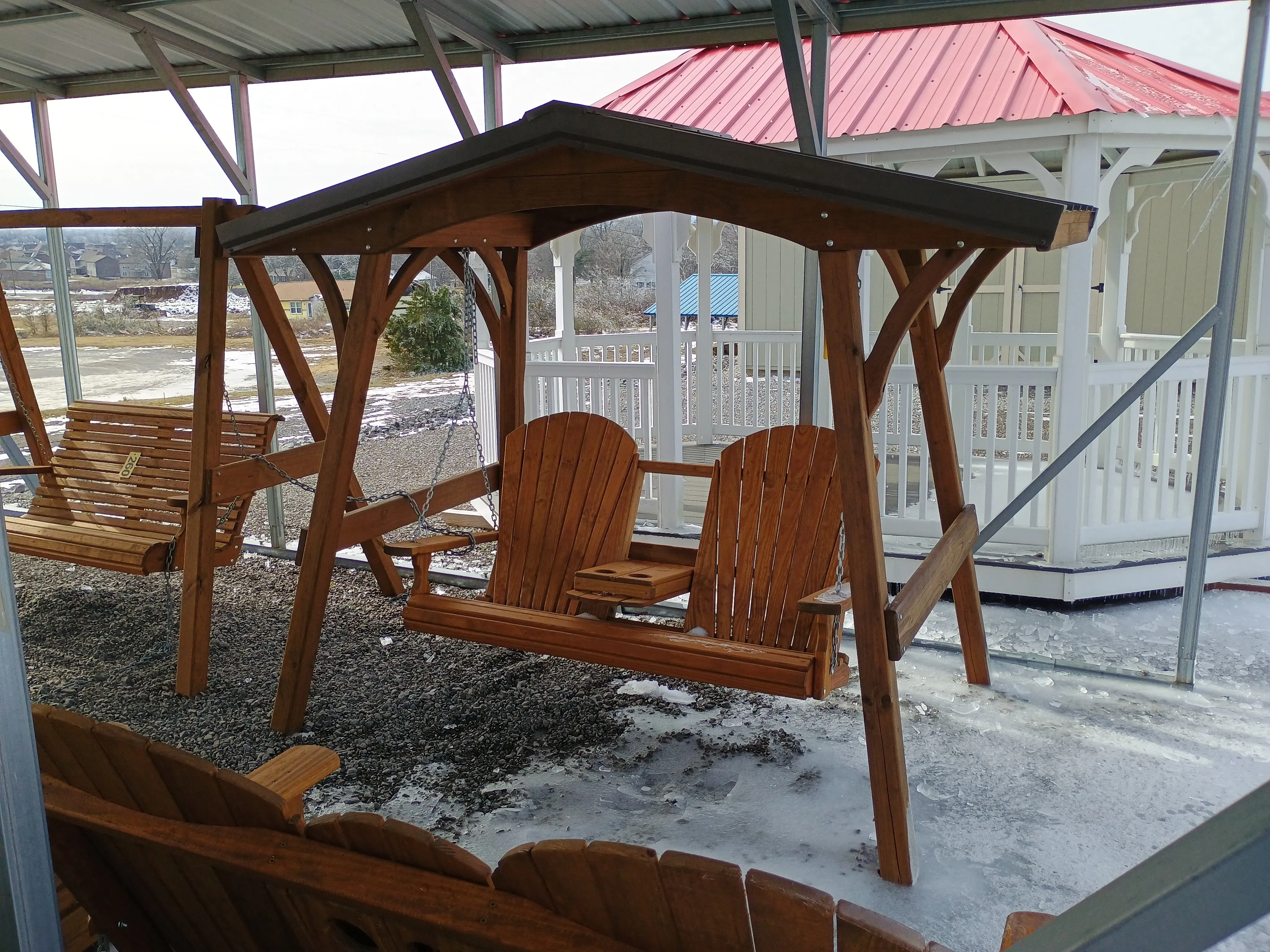 the front of a swing cover holding up a bench with chains. There is ice on the ground and a gazebo behind it.
