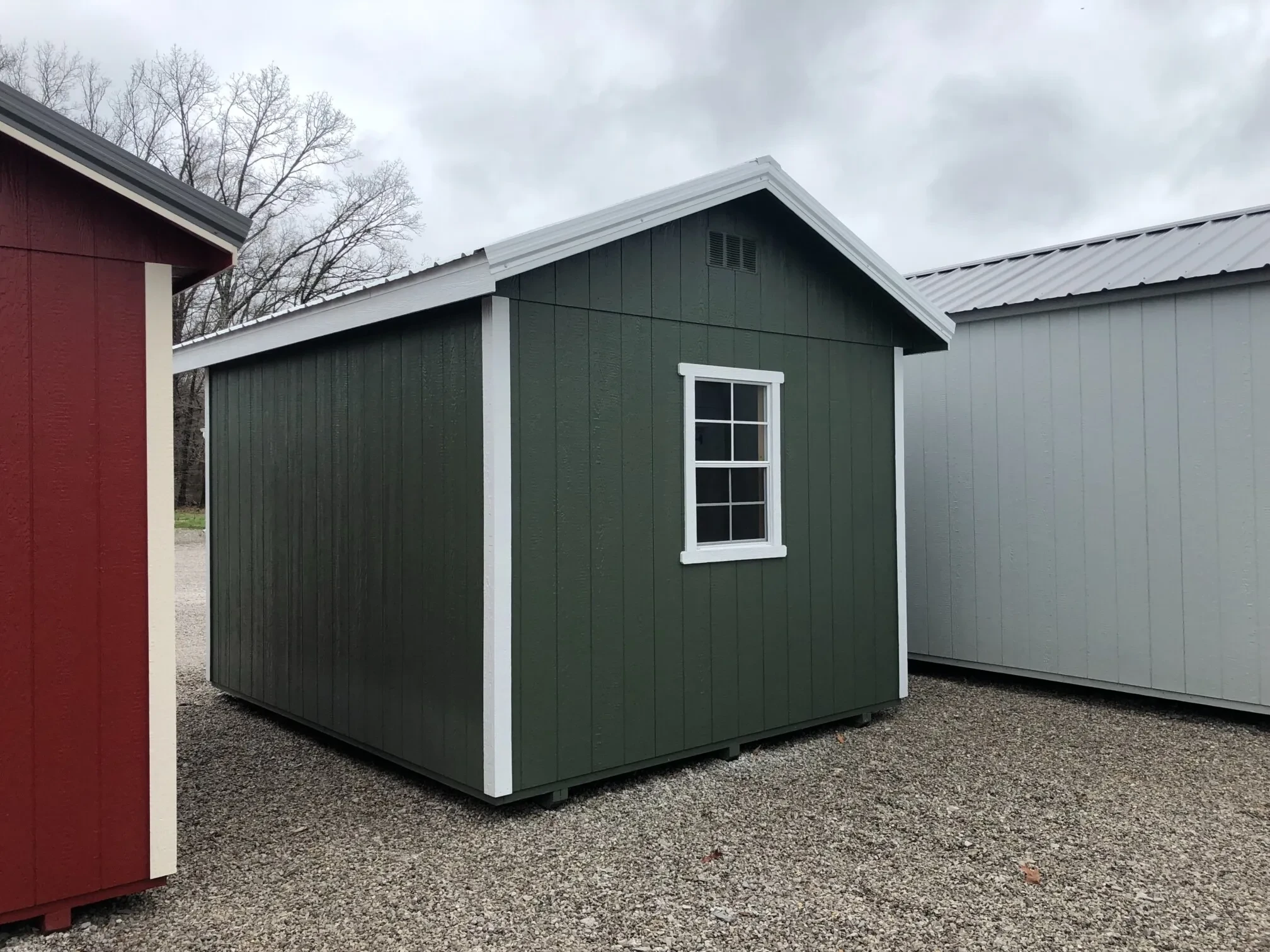 The back corner view of a green shed showing a window in the middle of the back wall.