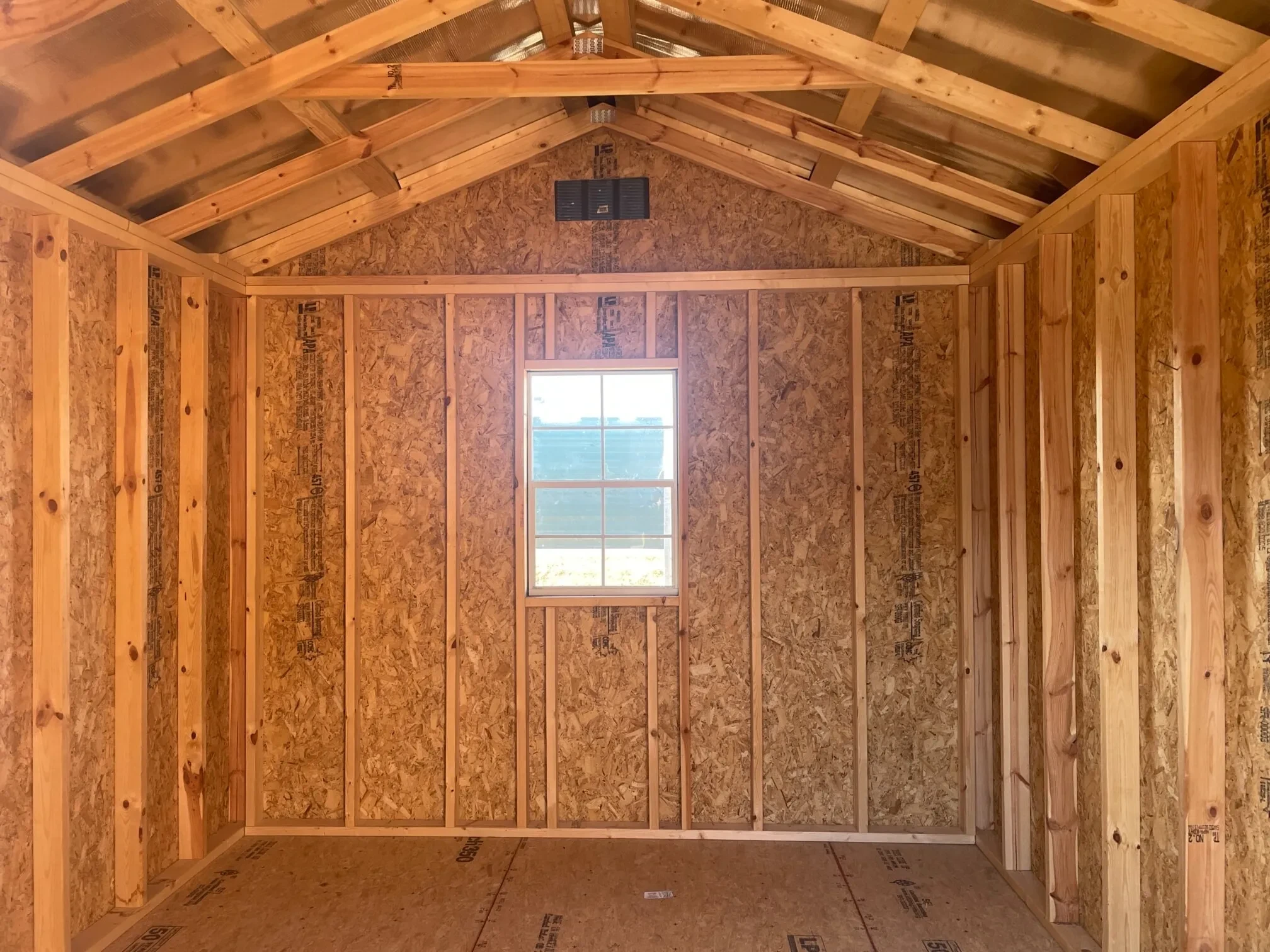 the inside of a wood utility shed looking at the back wall. There is a window in the middle of it