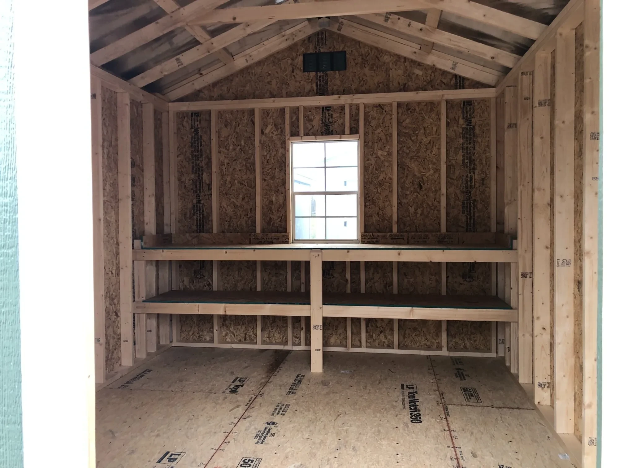 The inside of a wood shed that shows double shelves along the back wall and a window in the center