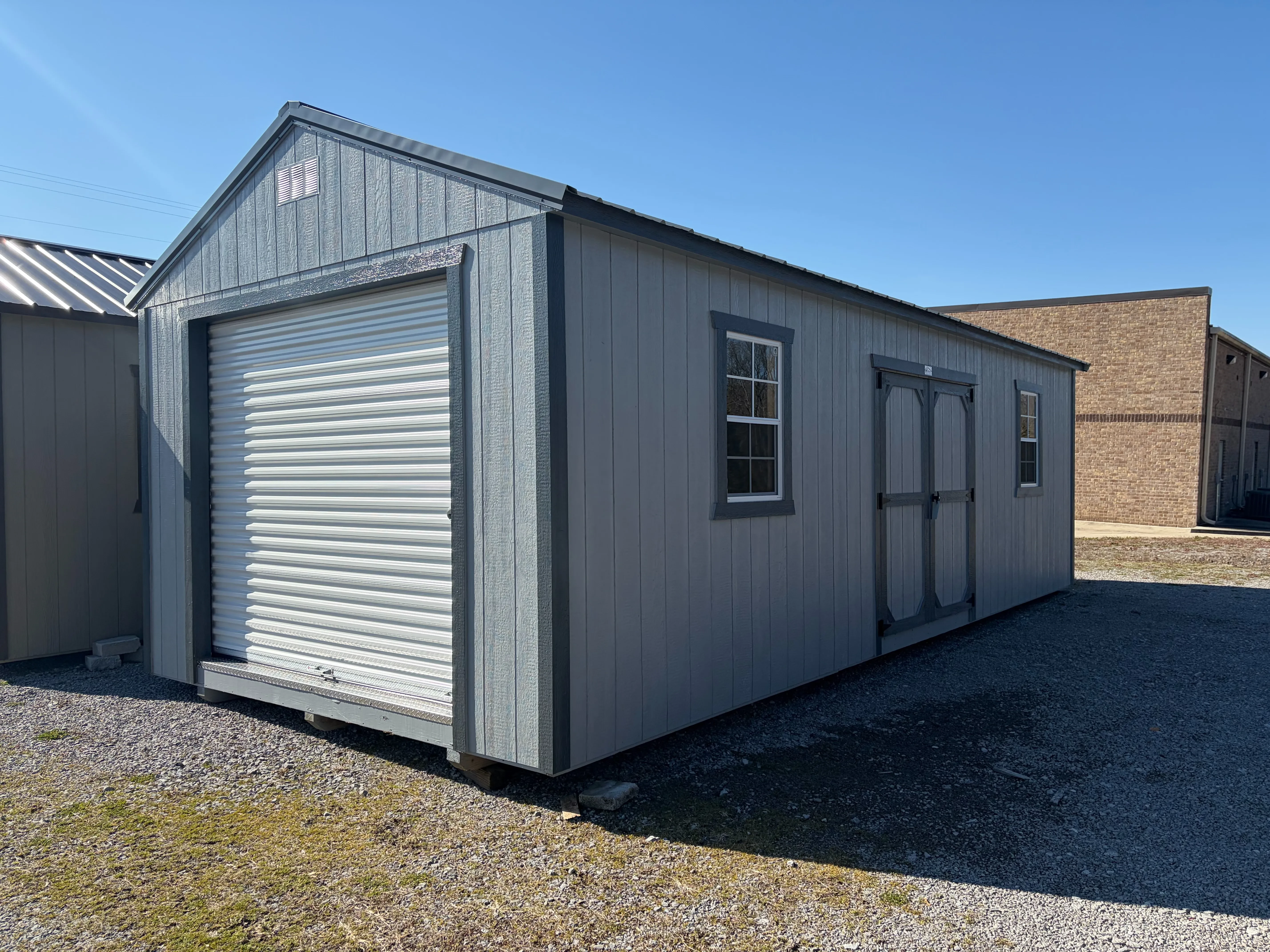 the light gray wood garage shed with a rollup door in the front and double doors and windows on the right side