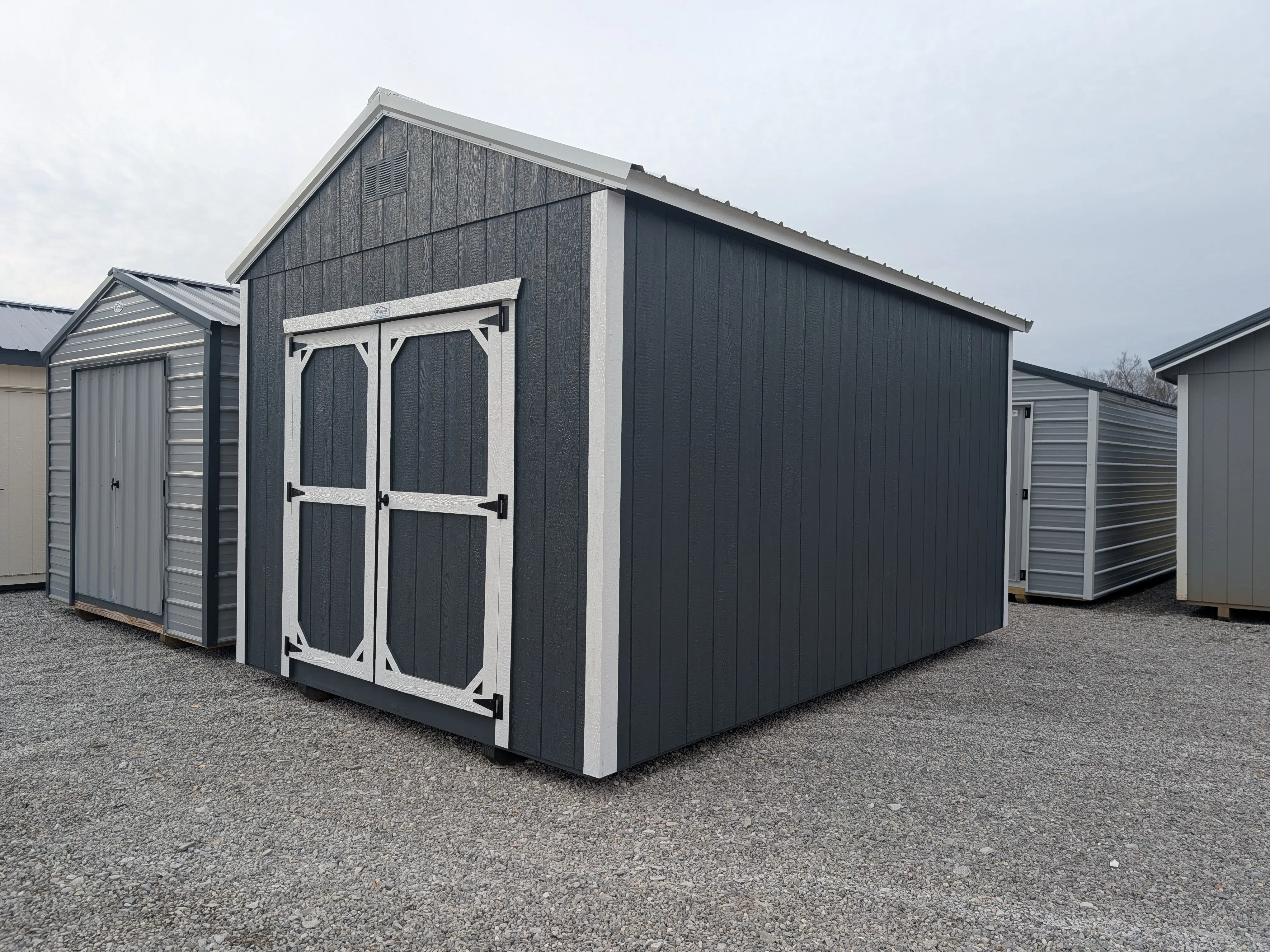 a wood utility shed with double doors. It is painted a slate gray color and has white trim