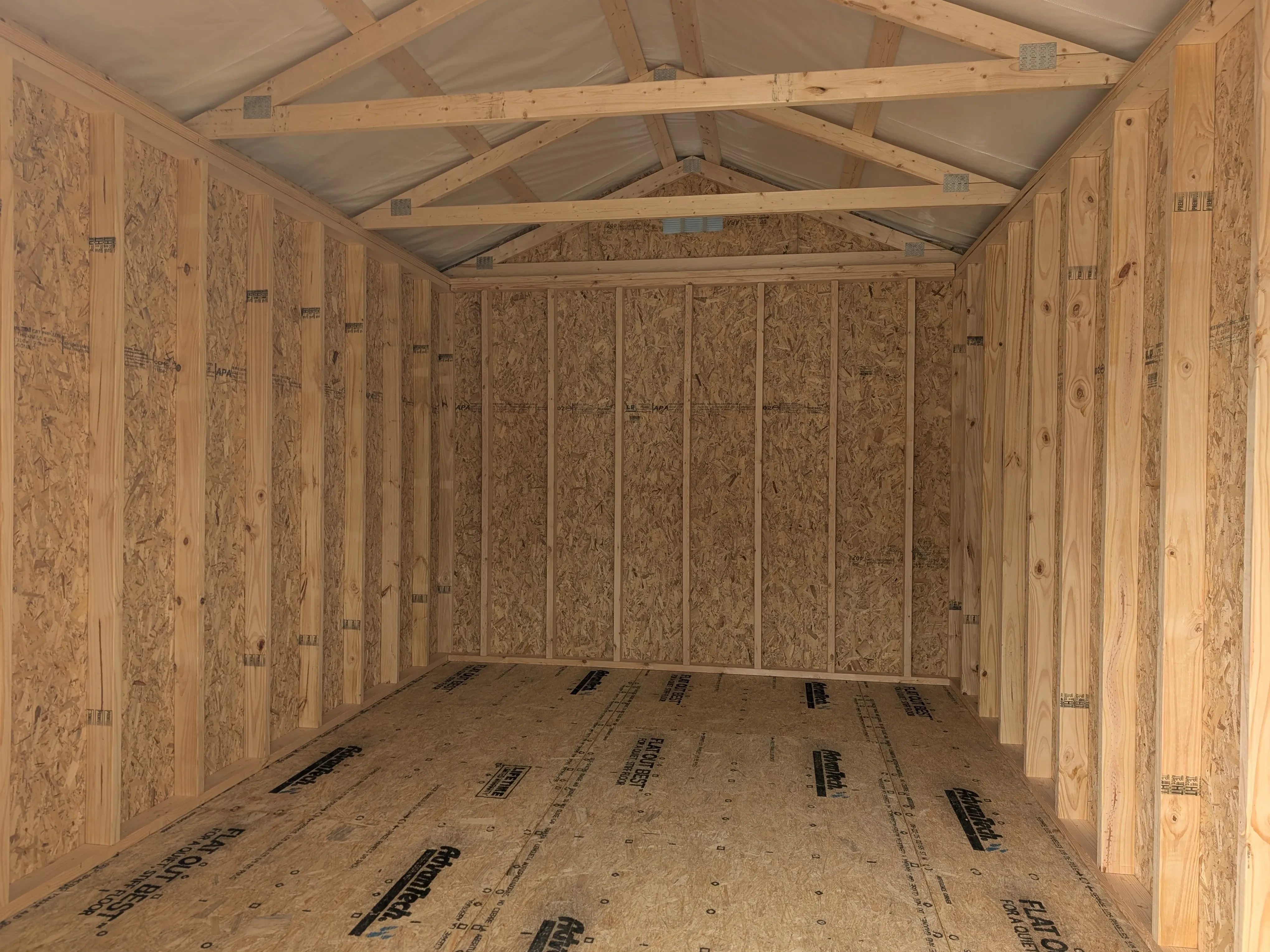 the inside of a wood utility shed. It shows the wood floor and the wood framing and trusses