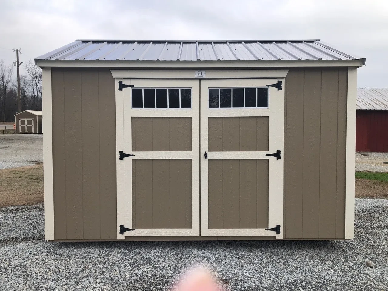 small buckskin wood shed with double doors that have transom windows in the doors with navajo white trim