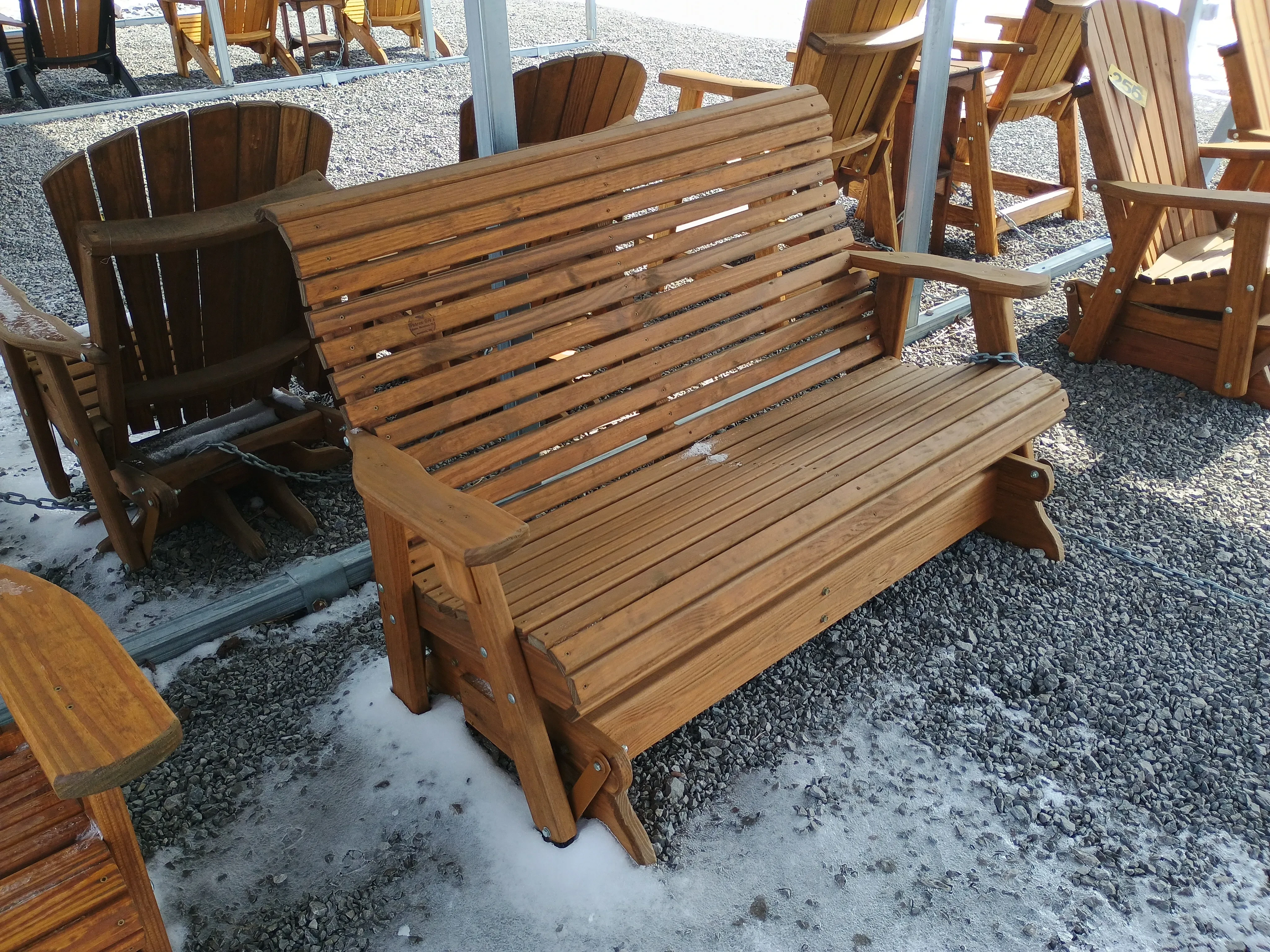 a wood stained bench with arm rests. It can glide back and forth. There are other chairs nearby