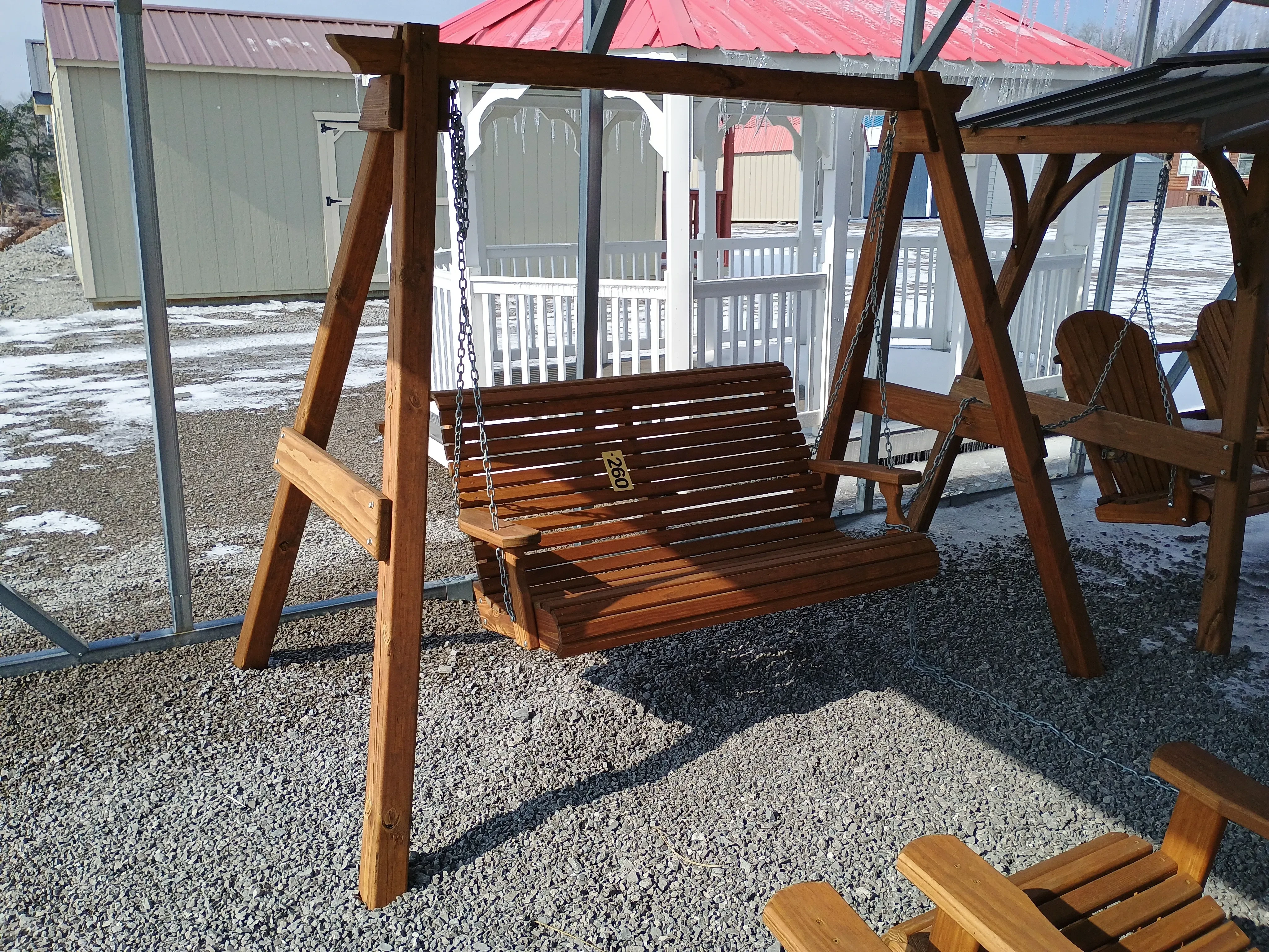 two a-frames holding up a wood swing by chains. There is other furniture nearby and ice and snow on the ground