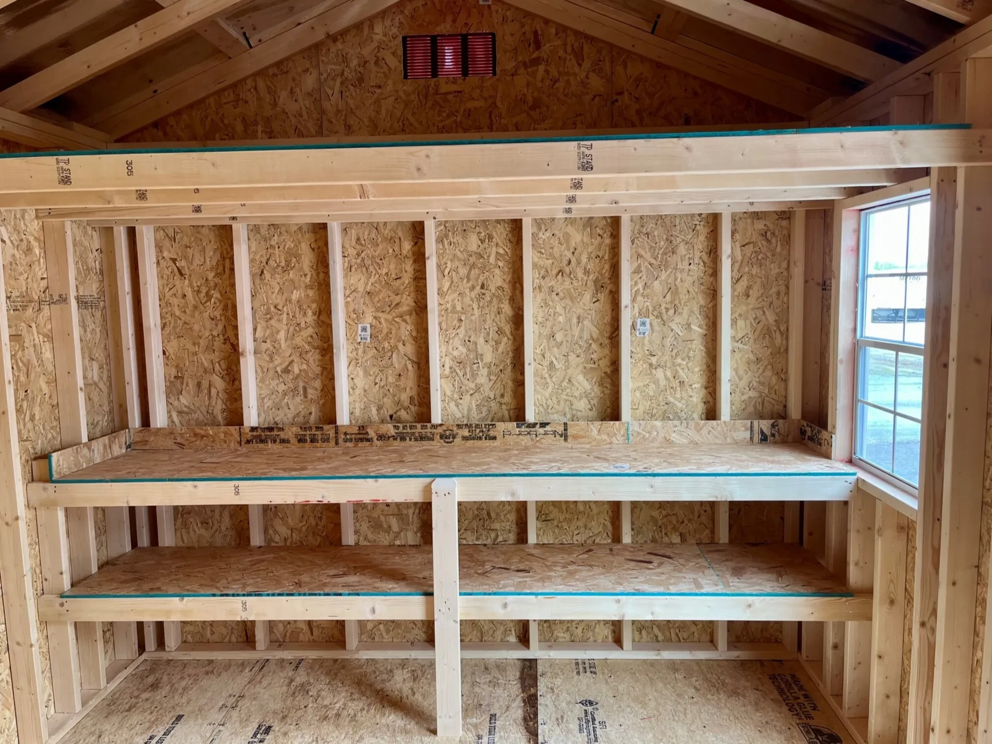 The interior of a wood shed showing double shelves and a window next to it