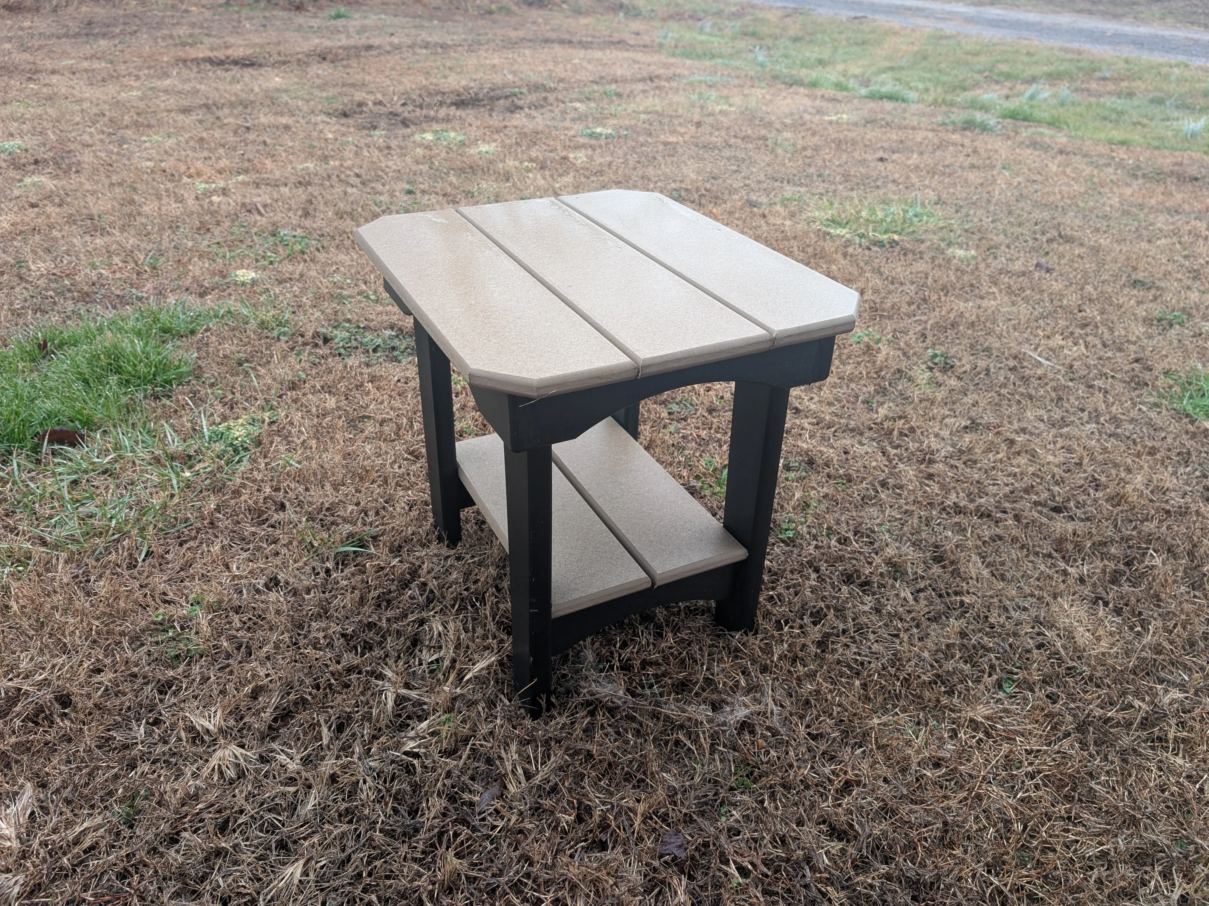 a polywood table, it is a weathered wood color with black legs, and it's sitting in the grass