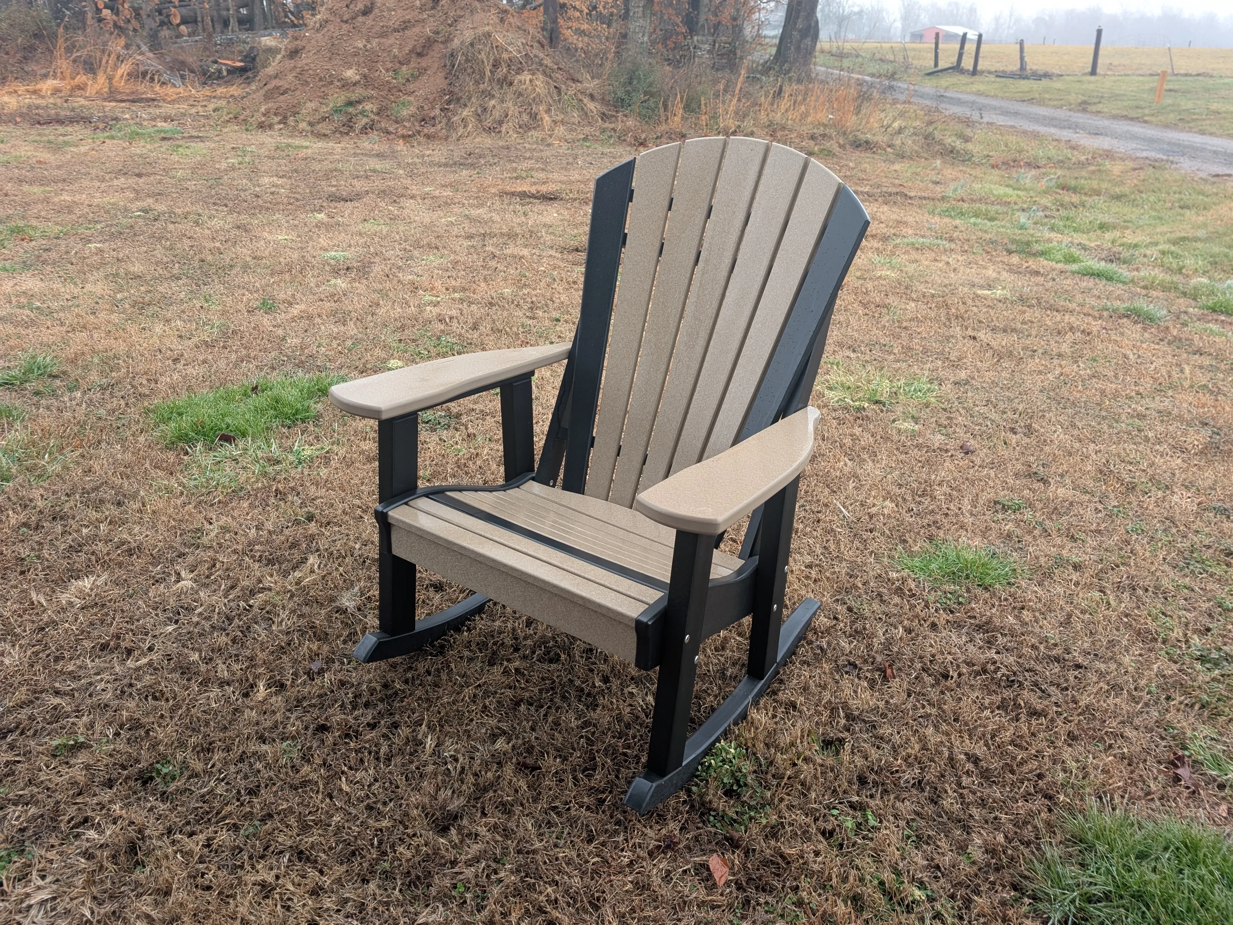 a rocking chair in the grass. It it a weathered wood color with black trim and rocker legs