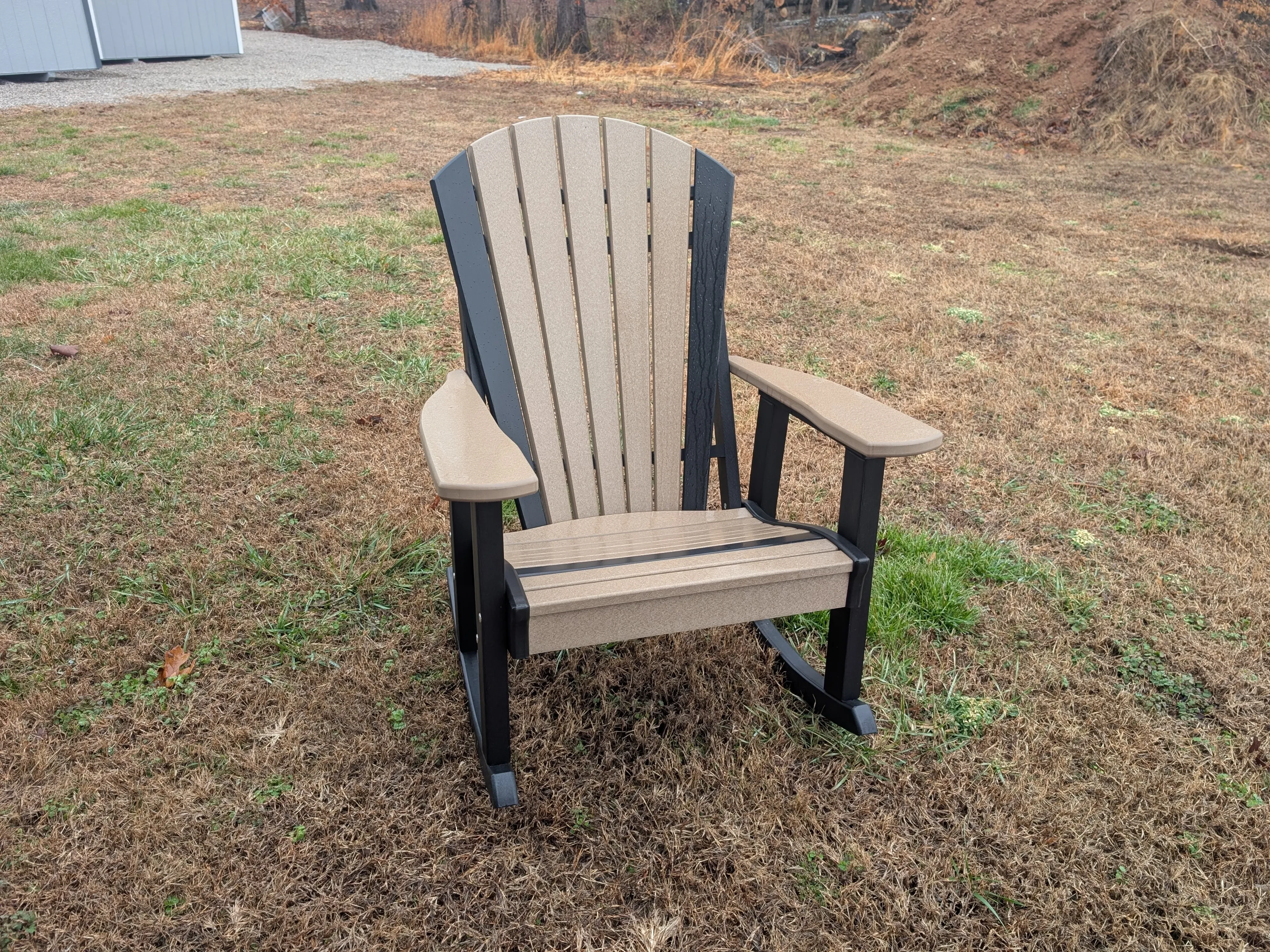 a rocking chair sitting in the grass. It is a weathered wood color with black legs