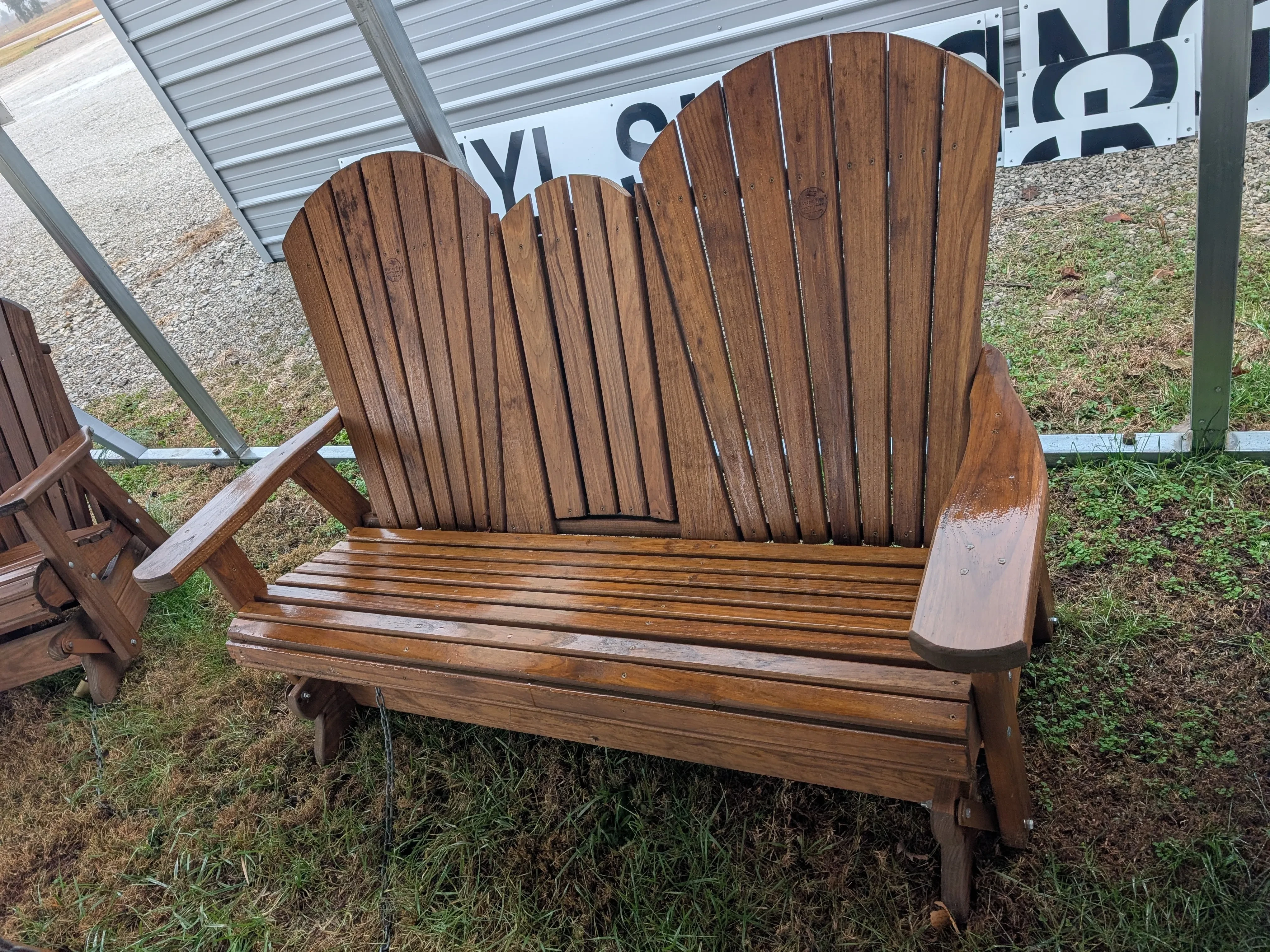 a wood stained and sealed bench sitting in the grass. it has a center console with cupholders in the upright position