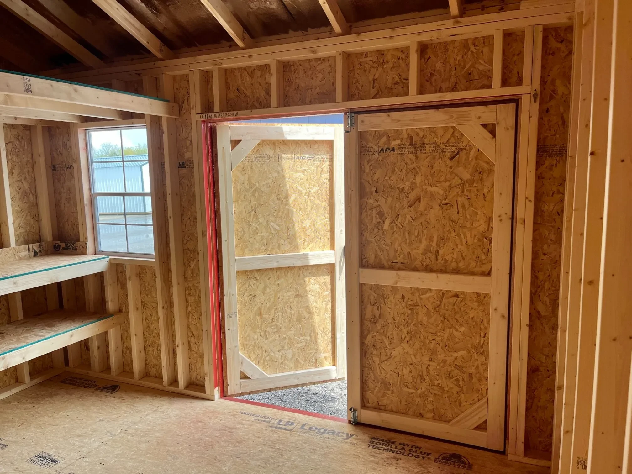 The inside of a wood shed showing the double shelves, a window, and double doors open