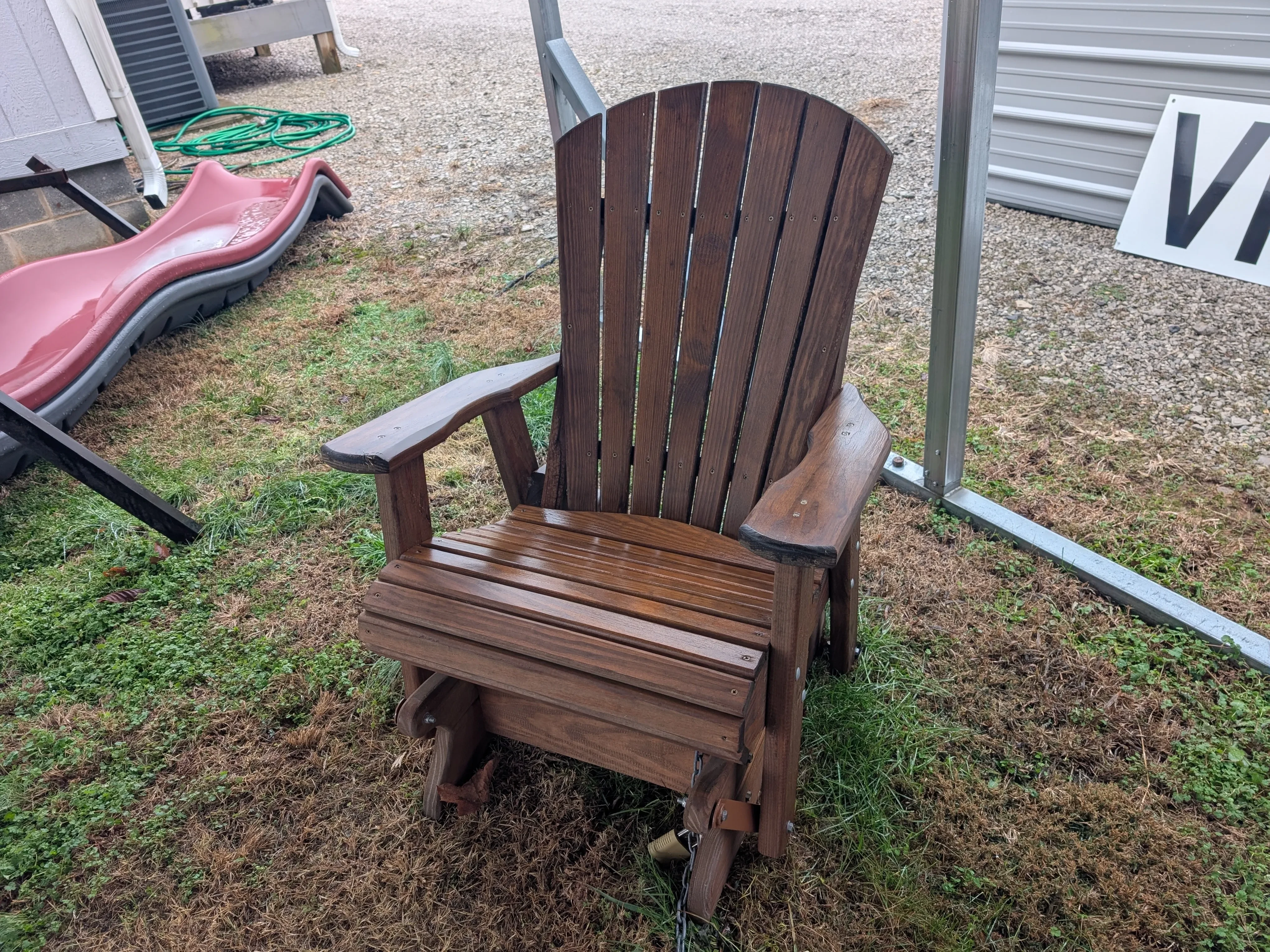 a wood chair sitting in the gras. It can glide back and forth and it has arm rests