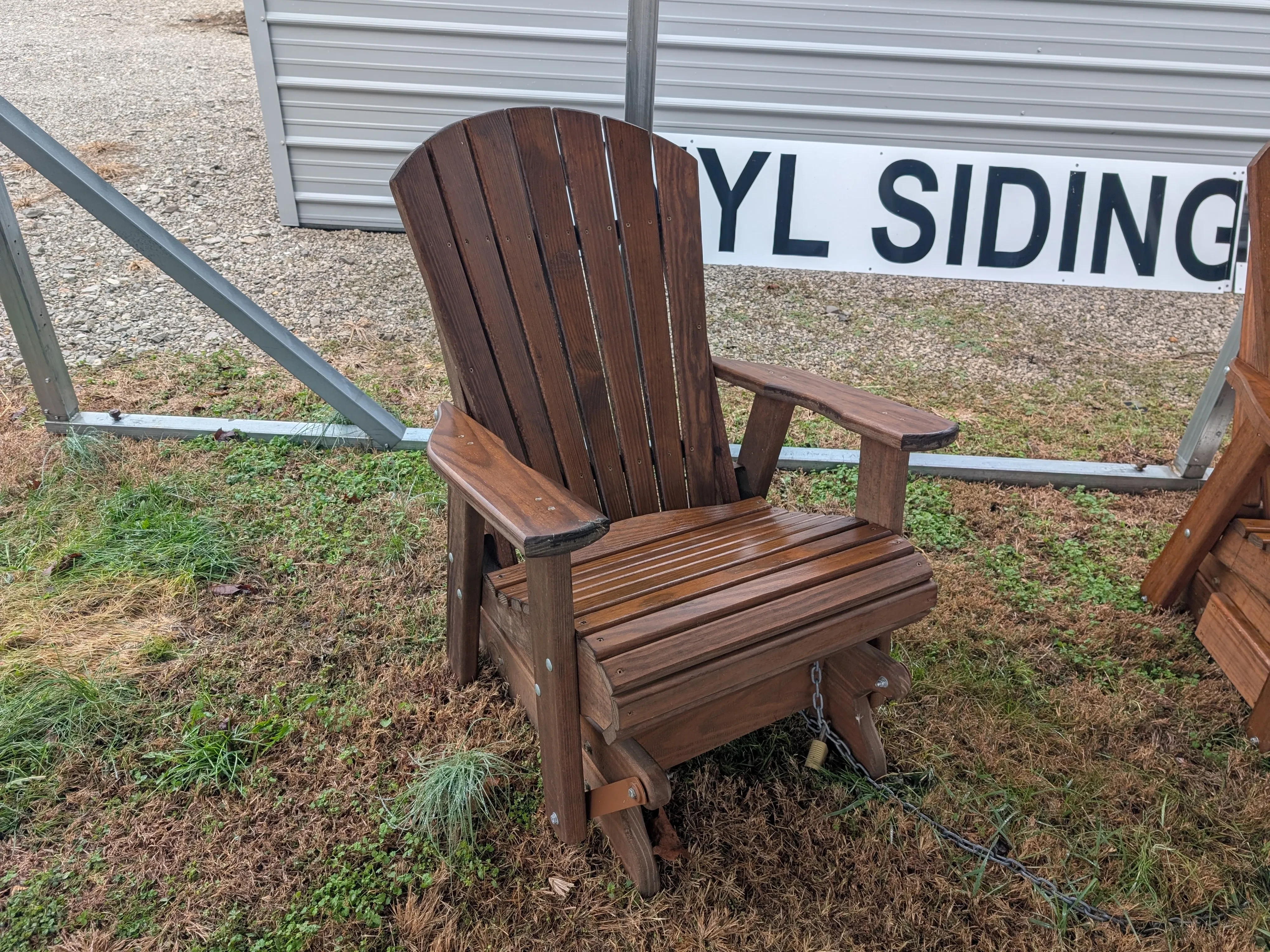 a wood stained chair sitting in the grass. It can glide back and forth and it has arm rests.