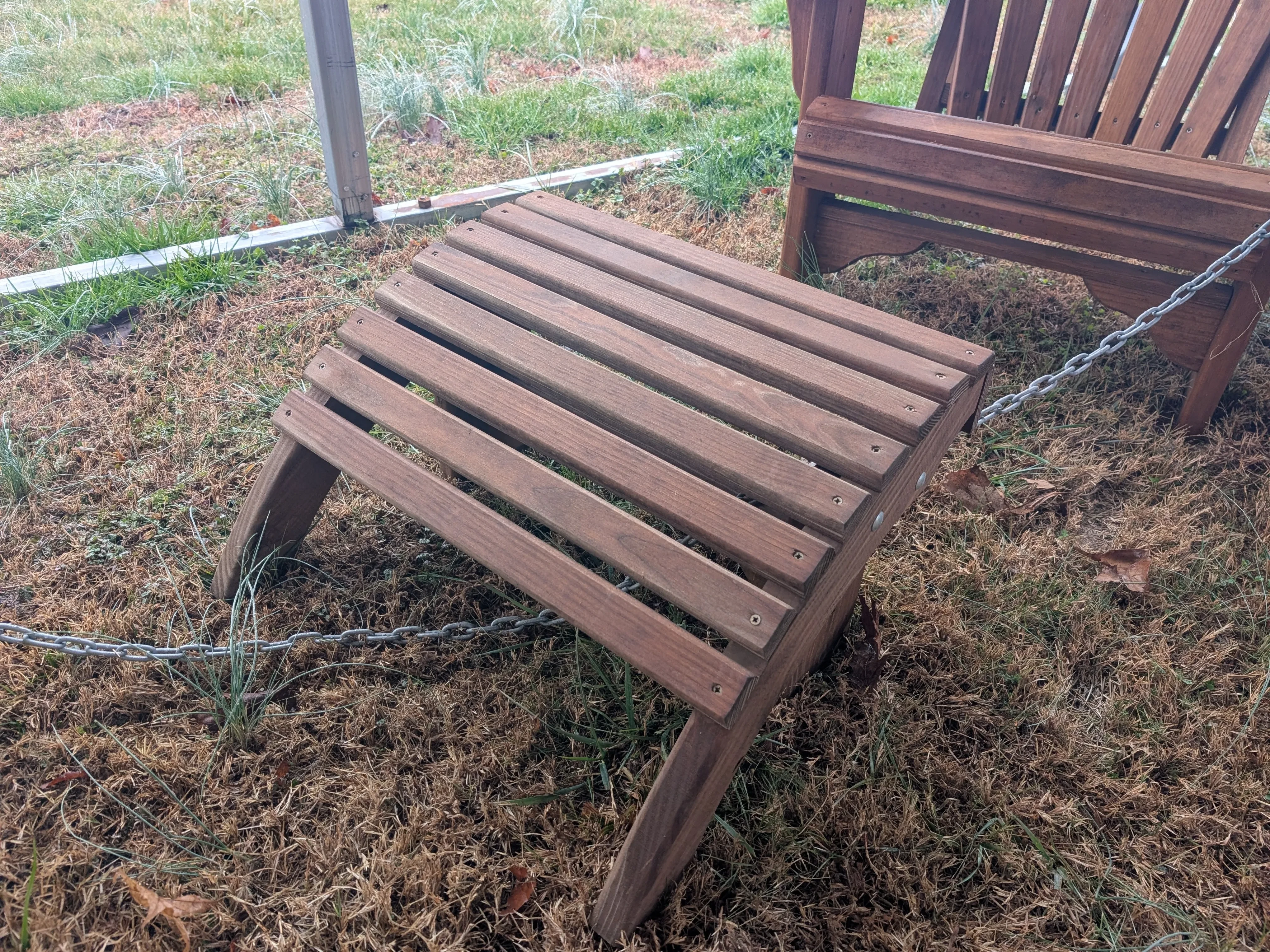 a wood footstool in the grass. It has eight horizontal planks making up the place where you set your feet