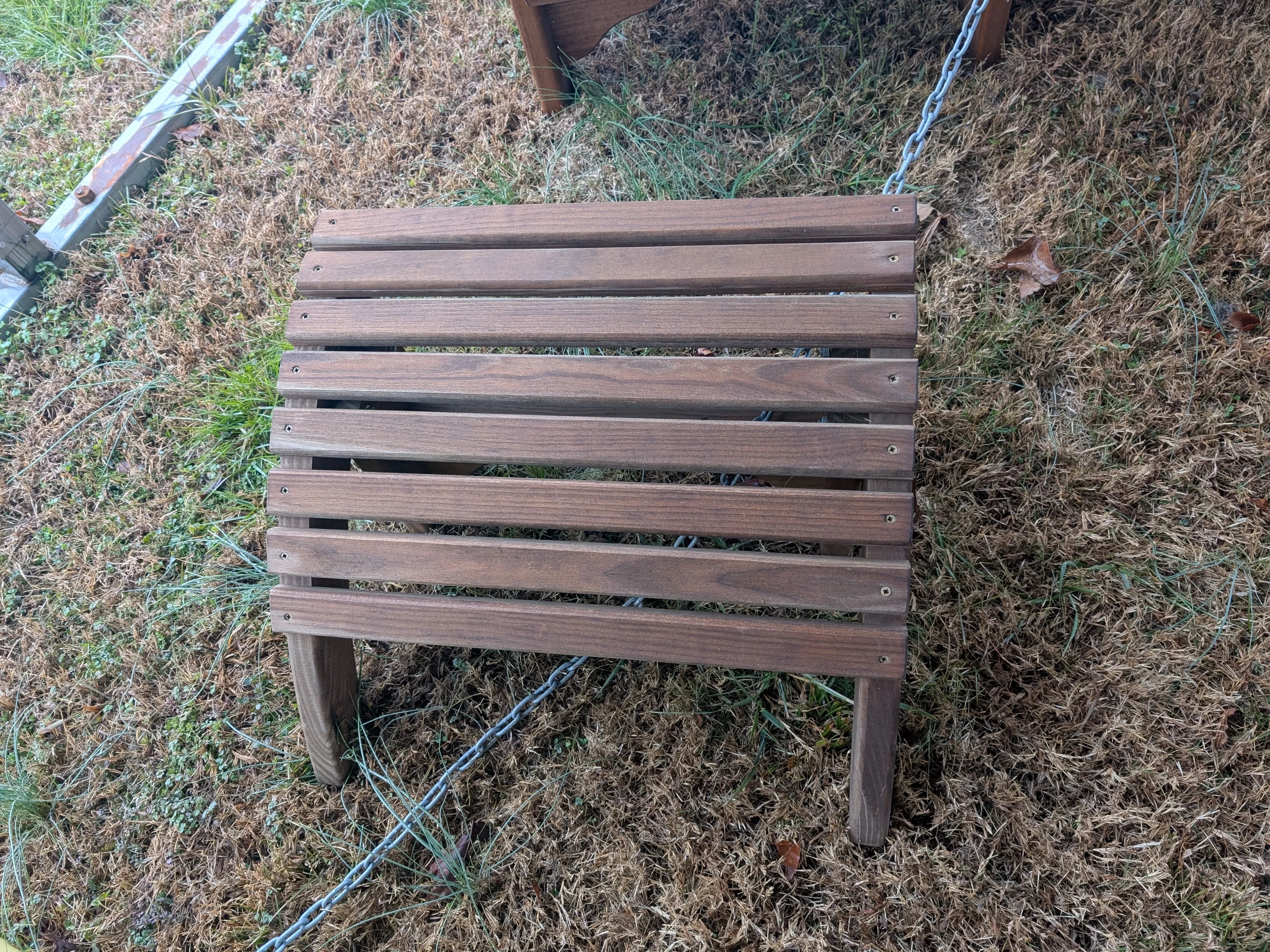 a wood stained foot stool in the grass chained up