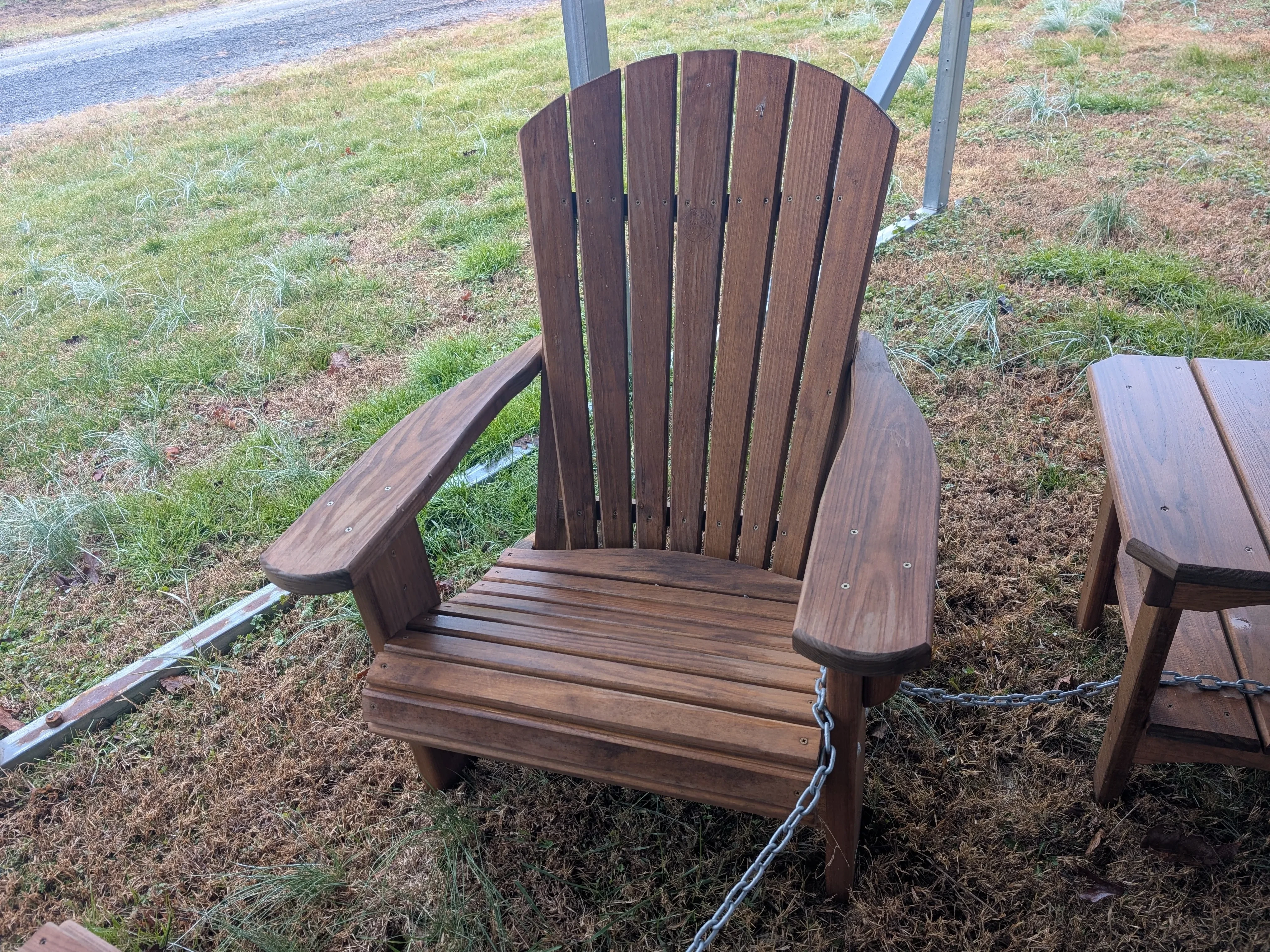 a wood stained and sealed chair chained up in the grass. It has armrests